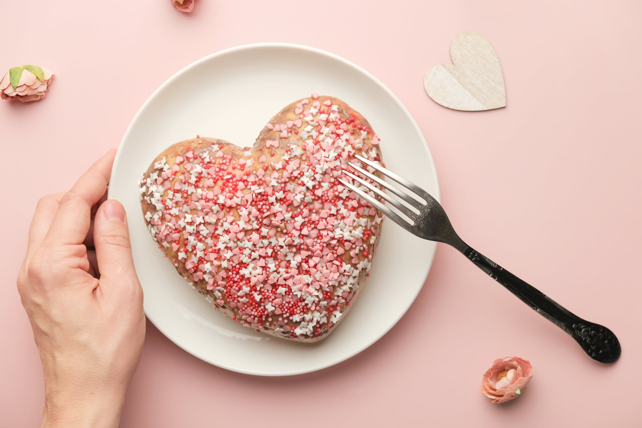Valentines Day food, festive dinner. Female hand holds plate with heart shaped cake on pink background. Single young woman celebrating Valentine's Day.