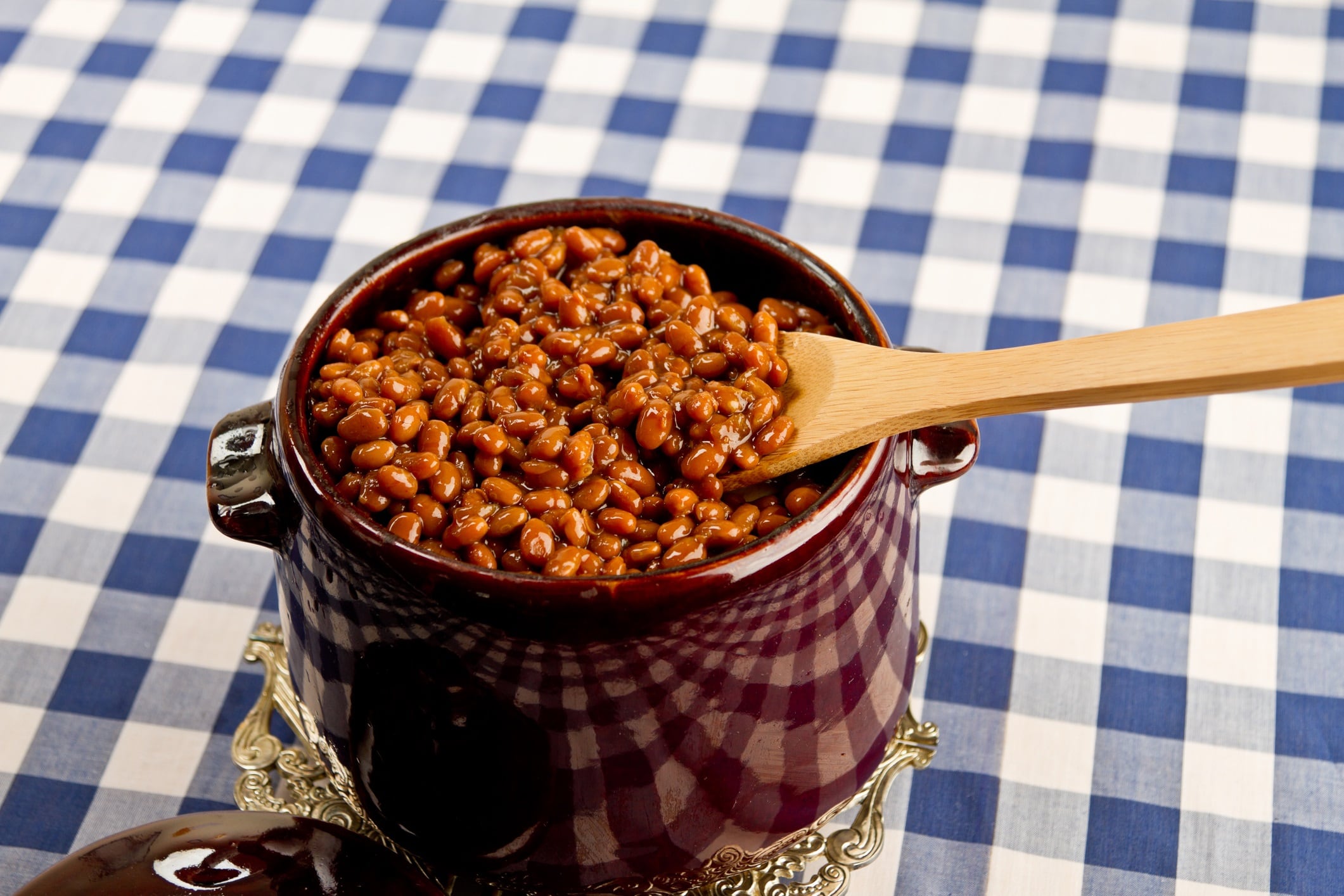 Pot of baked beans on a blue gingham tablecloth.