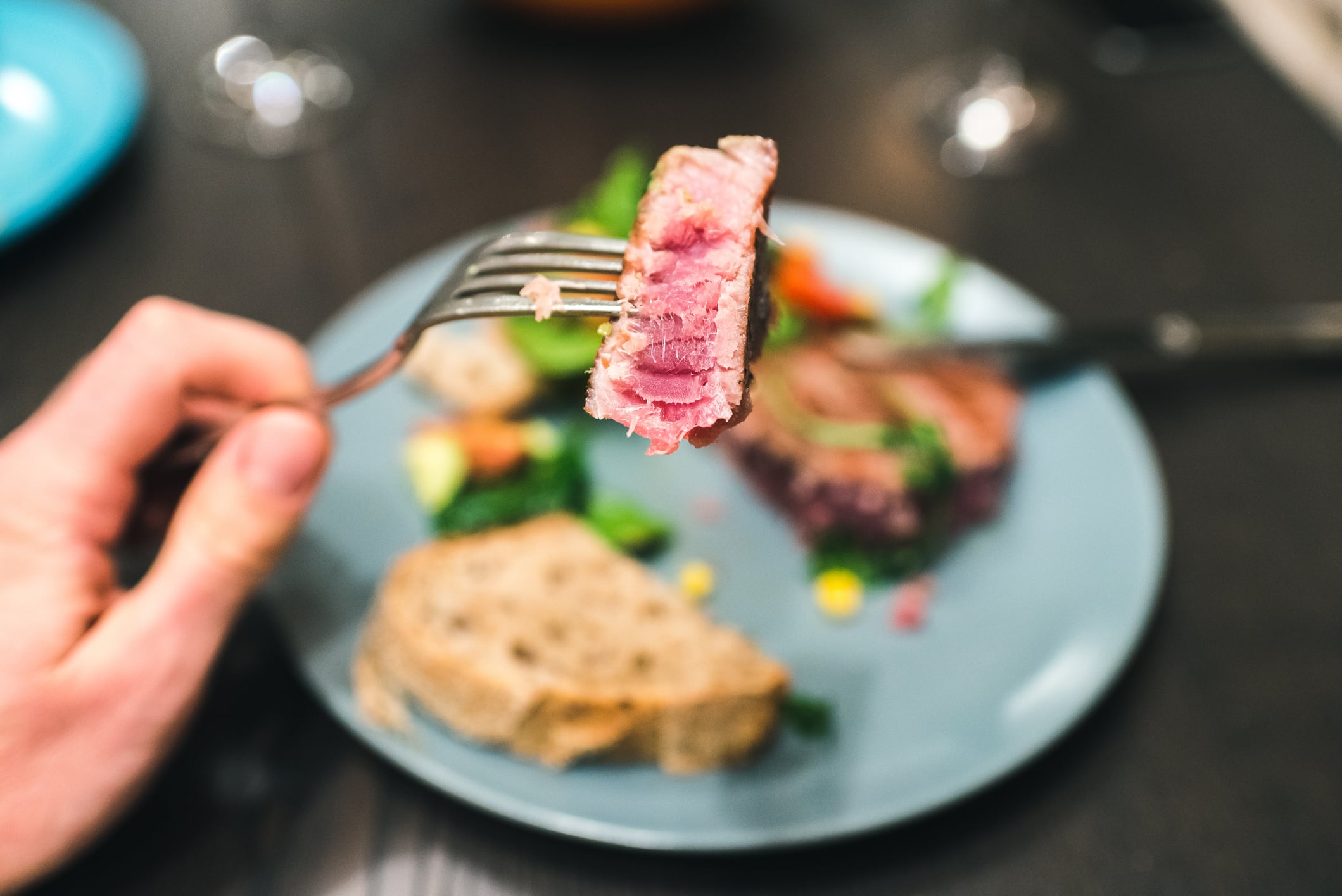 Slice of medium rare prepared tuna steak on a fork in the foreground. The whole tuna steak in the background blurred.