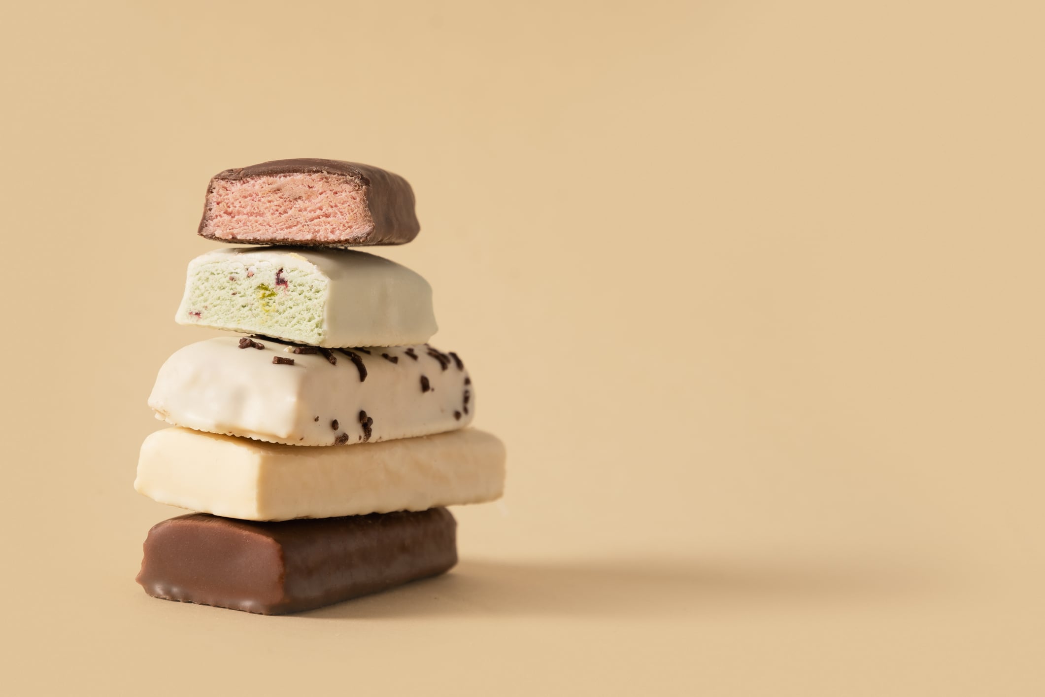 Different whey protein bars with various coatings and sprinkles on beige background. Close up. Copy space.