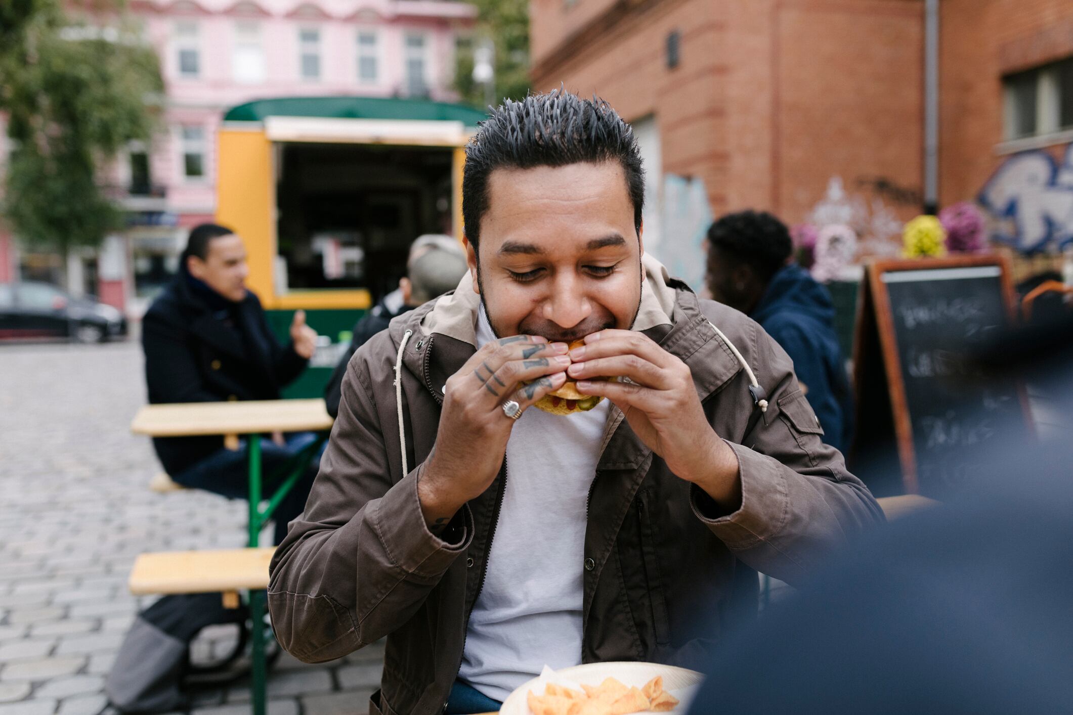 A man eating a burger while sitting outdoors at a food truck eatery.