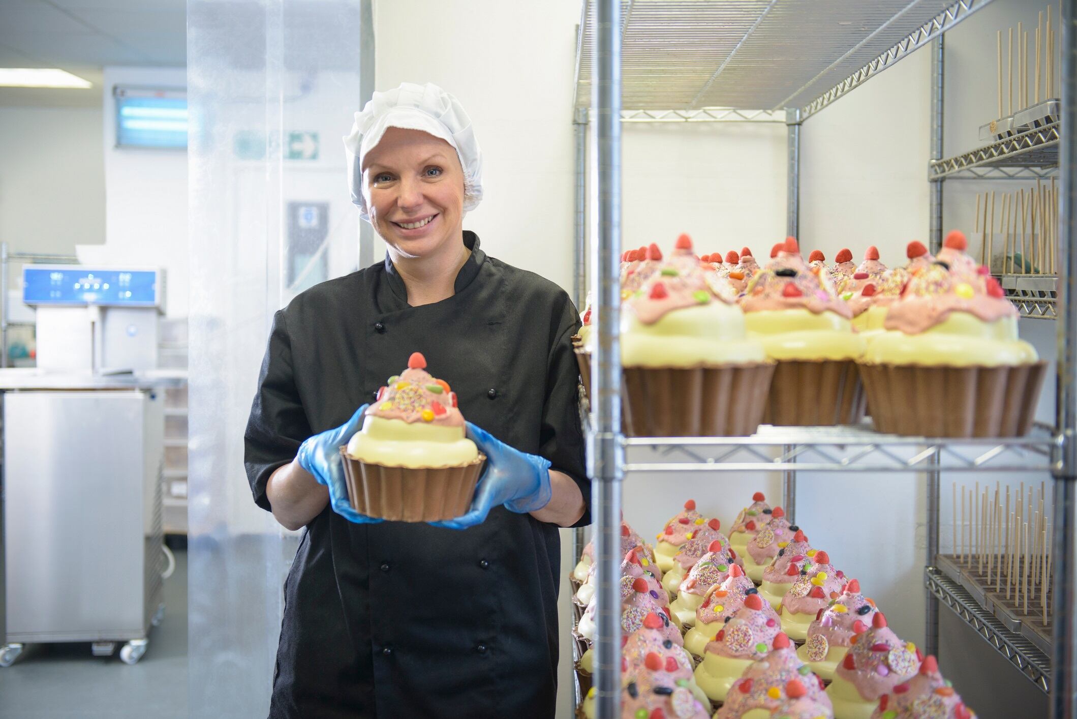Portrait of chocolatier holding large chocolate cup cake in chocolate factory