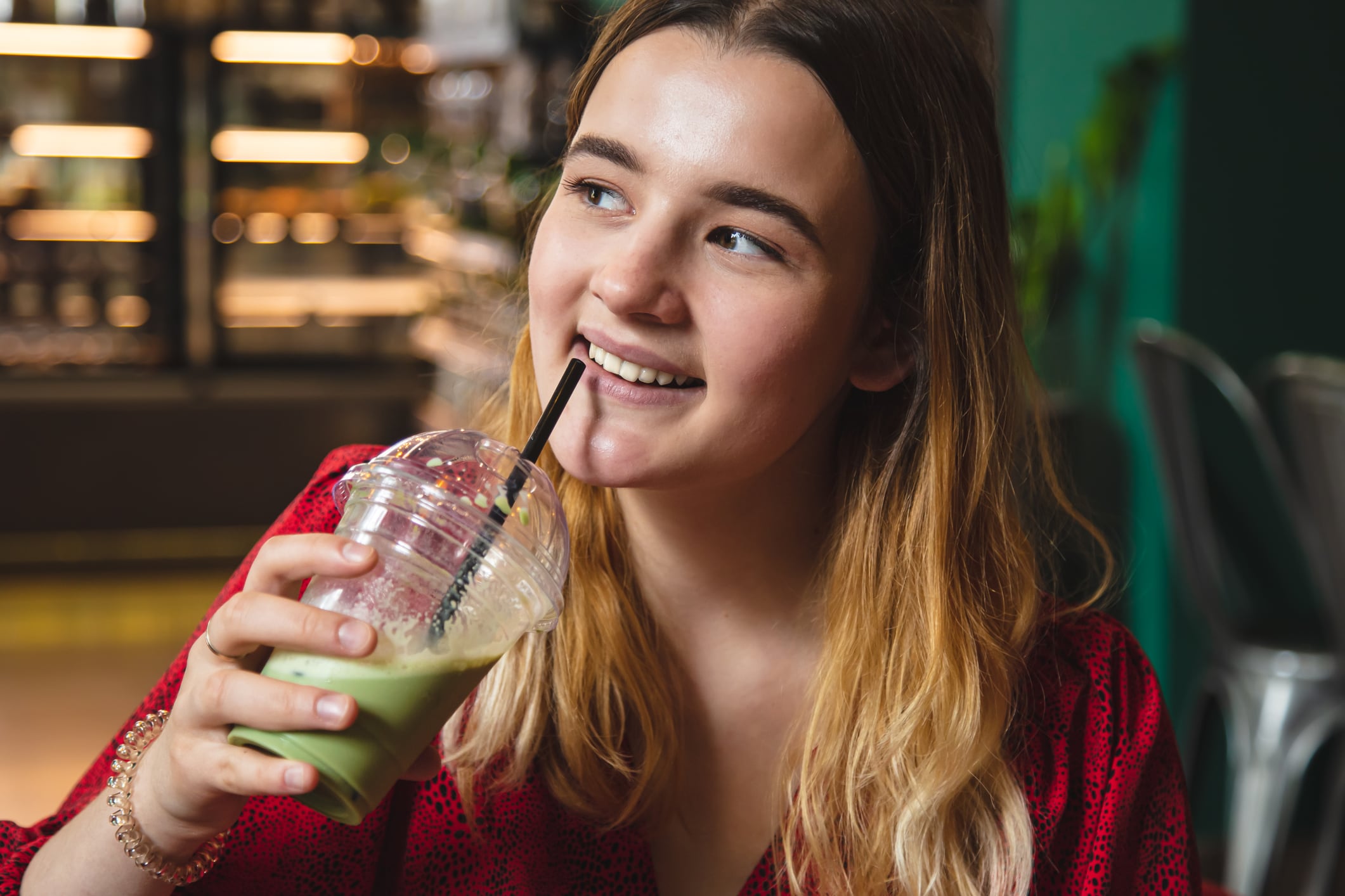 A young woman in a red dress in a cafe drinks a summer green drink ice latte.
