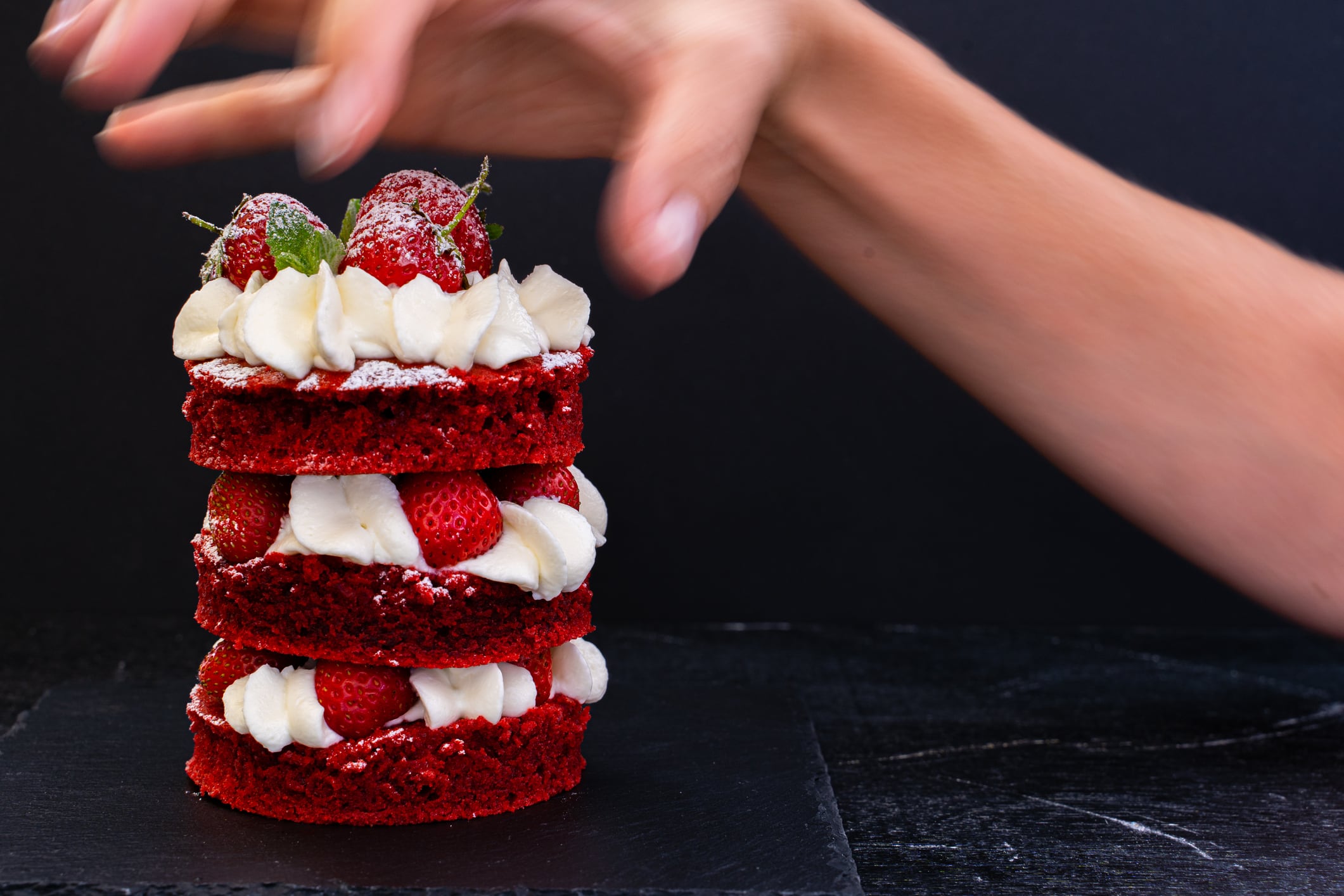 A woman's hand moves blurry out of focus grabbing the cake. Concept. The desire to eat sweets and fatty foods. The temptation of cake.