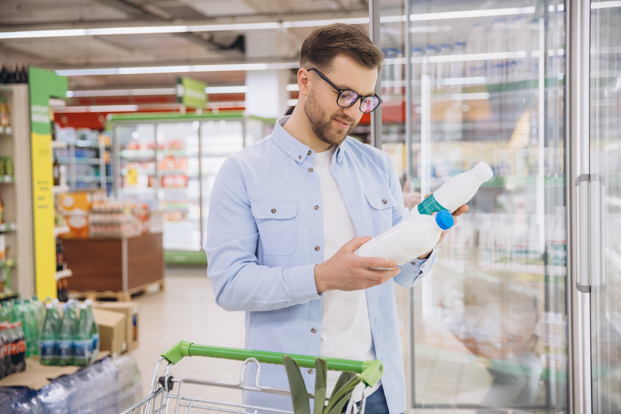 Man choosing a milk bottle in refrigerated section of a grocery store, comparing labels and ingredients for best choice