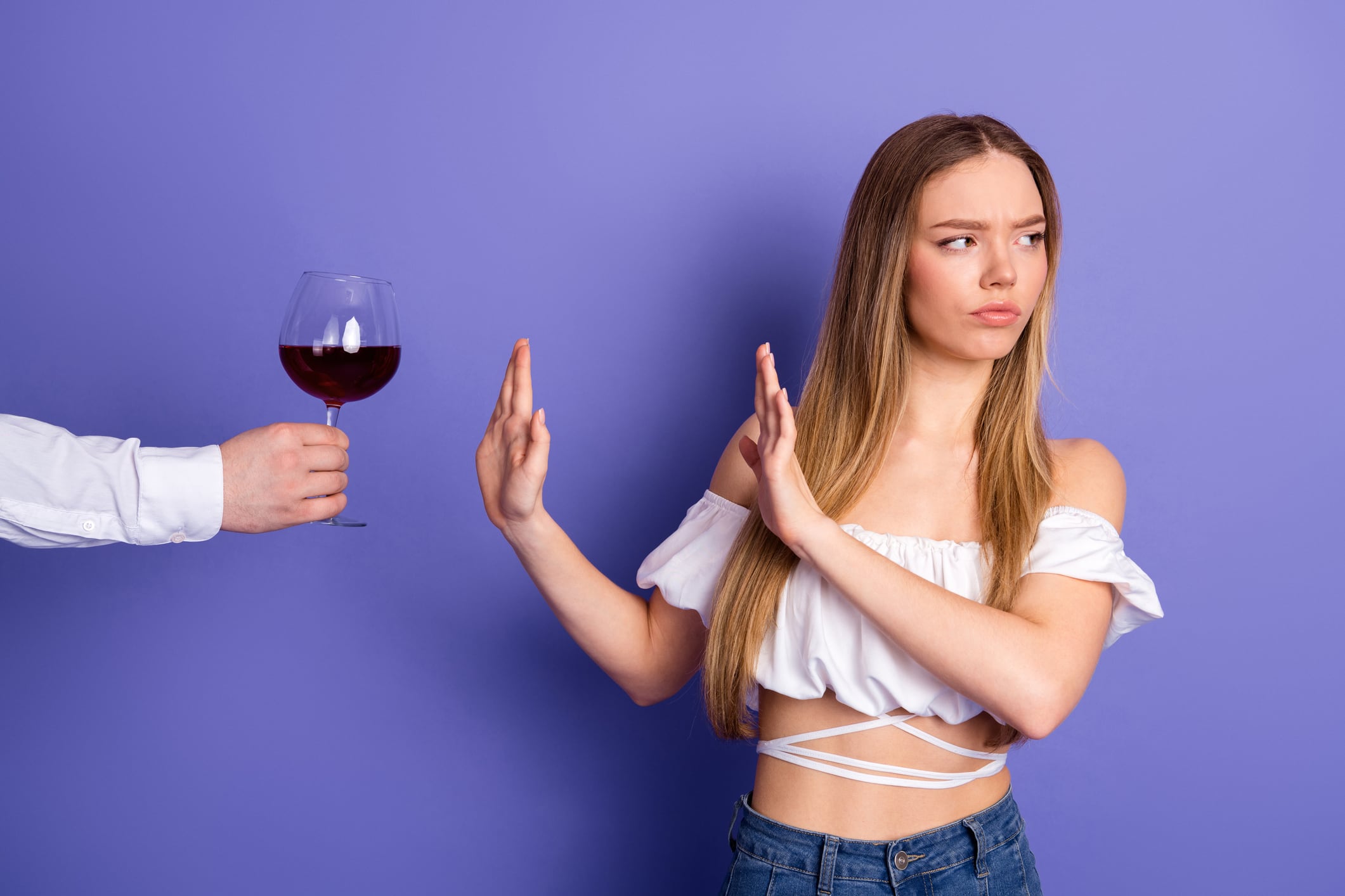 Depicting a refusal of wine from a stylish young woman in a casual outfit against a vivid purple background.
