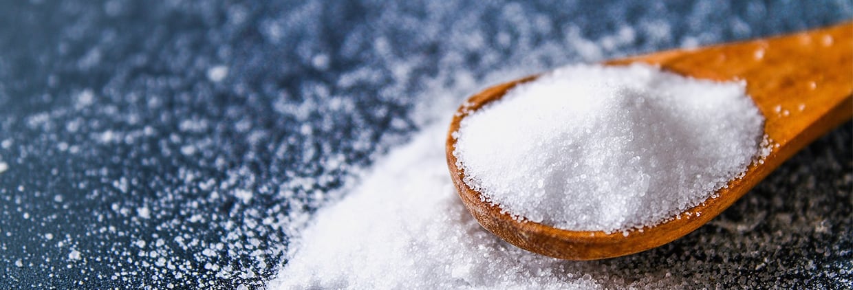 Crystals of shallow salt in a scoop, spoon on a dark gray table. Background for advertising salt. Table salty. Salted food