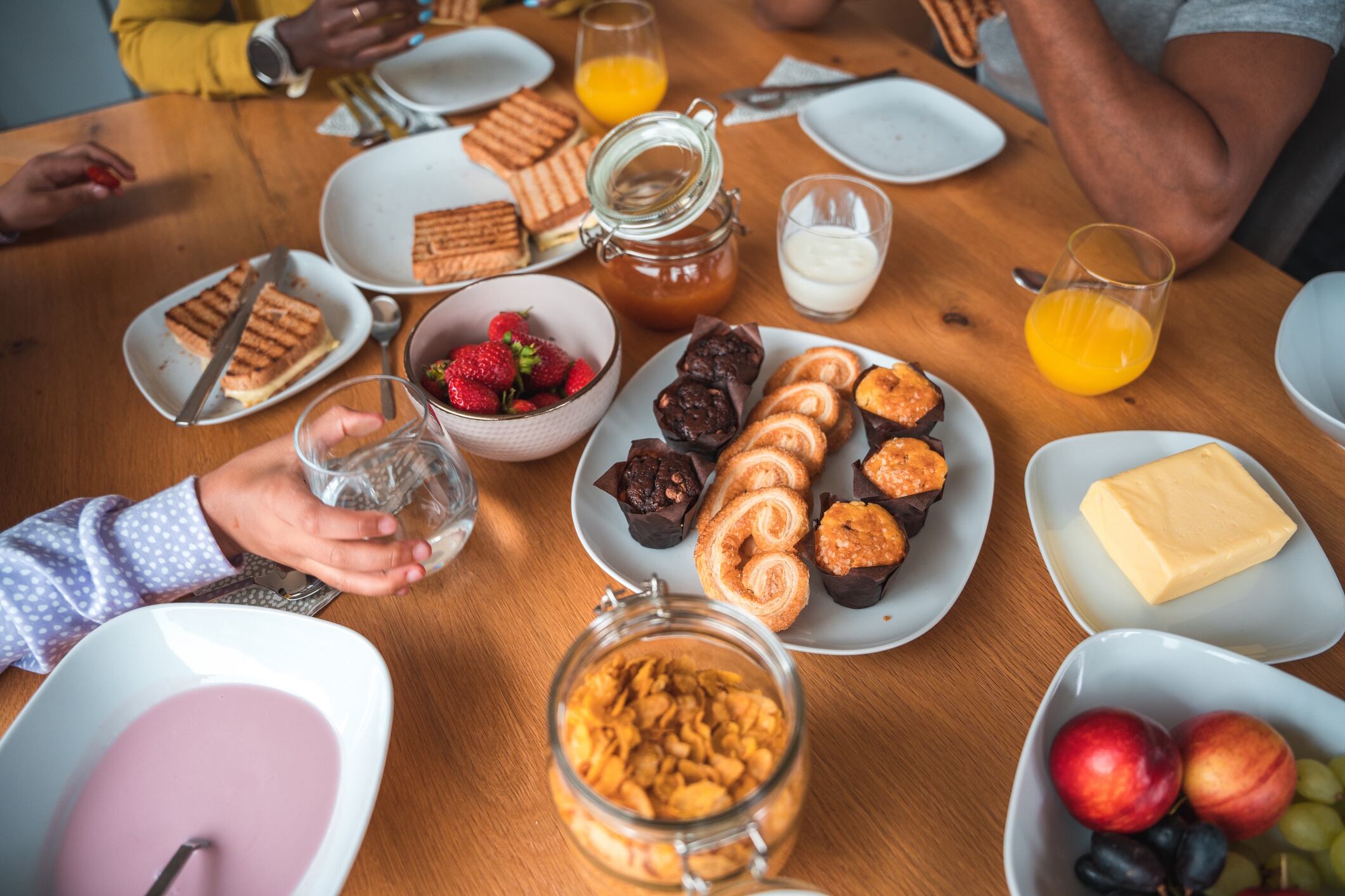 Mixed race family having a diverse breakfast at home. Table with fruits, cereals, yogurt, natural juices, sandwiches and pastry. AzmanL GettyImages
