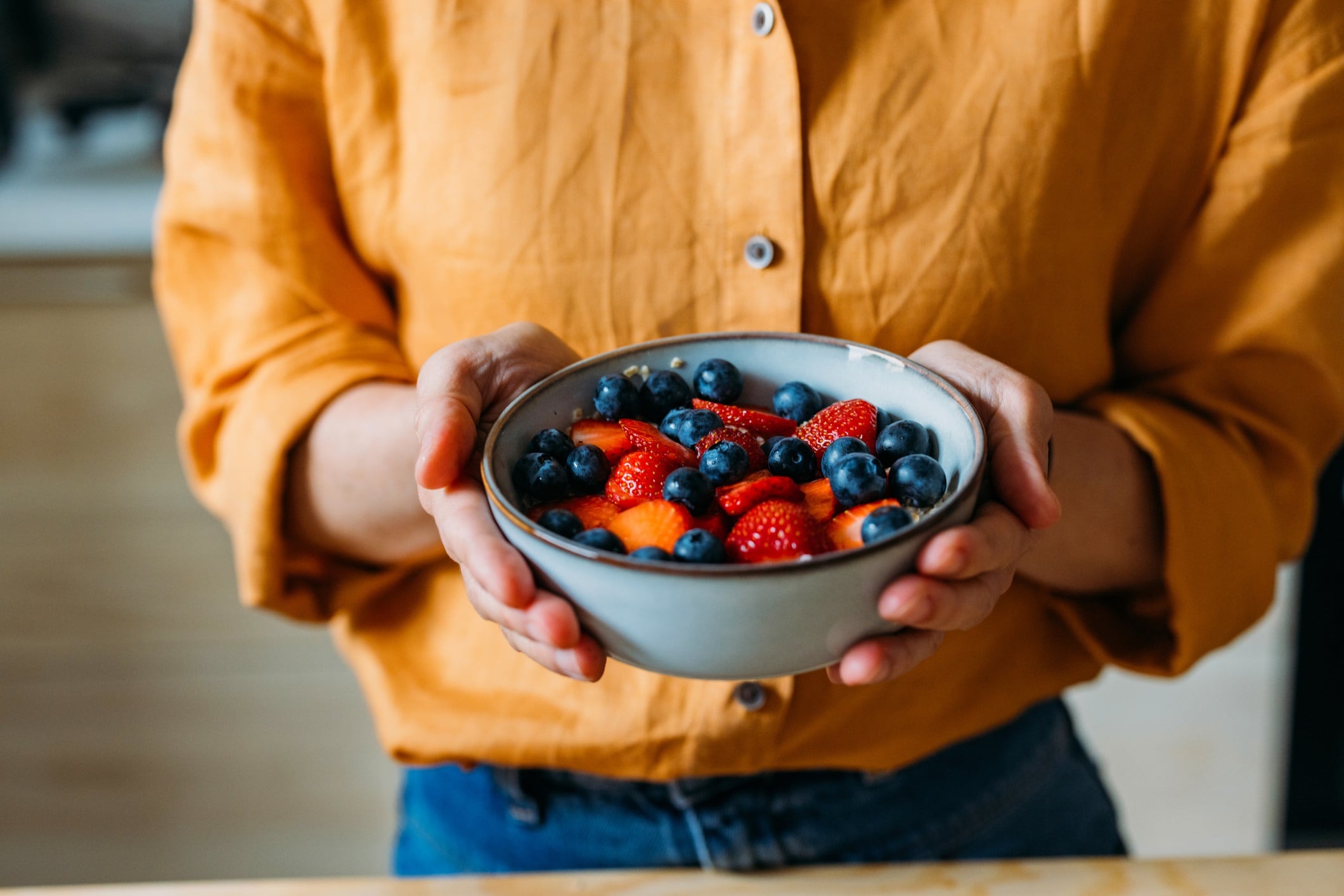A close-up of a person holding a bowl filled with fresh strawberries and blueberries, signifying healthy eating and freshness.