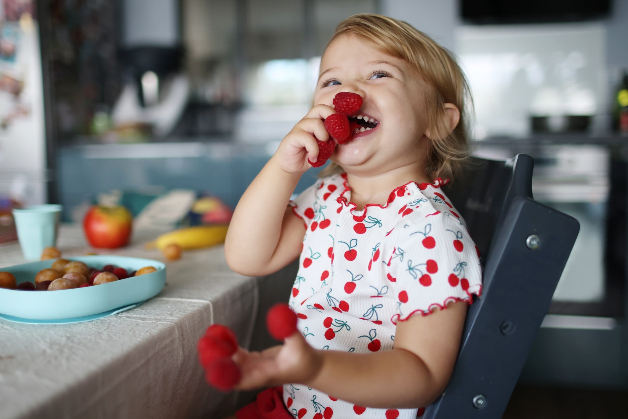 A 2 year old little girl eating raspberries at home.