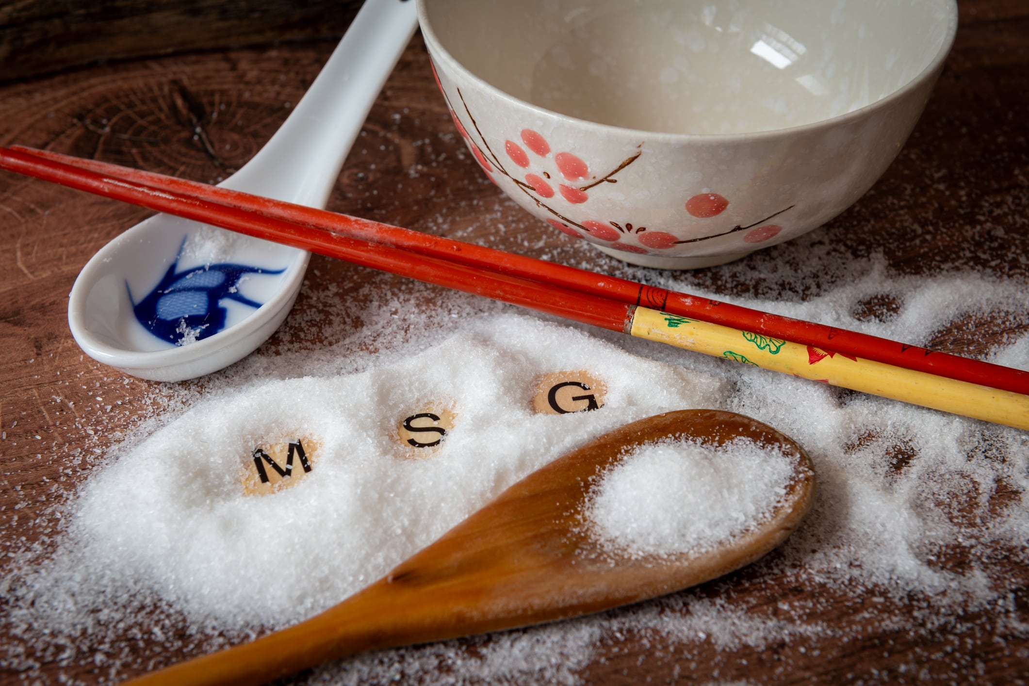 A rice bowl, ceramic spoon and a pair of chopstick on a kitchen work top with a heap of monosodium glutamate with the letters M S G.
