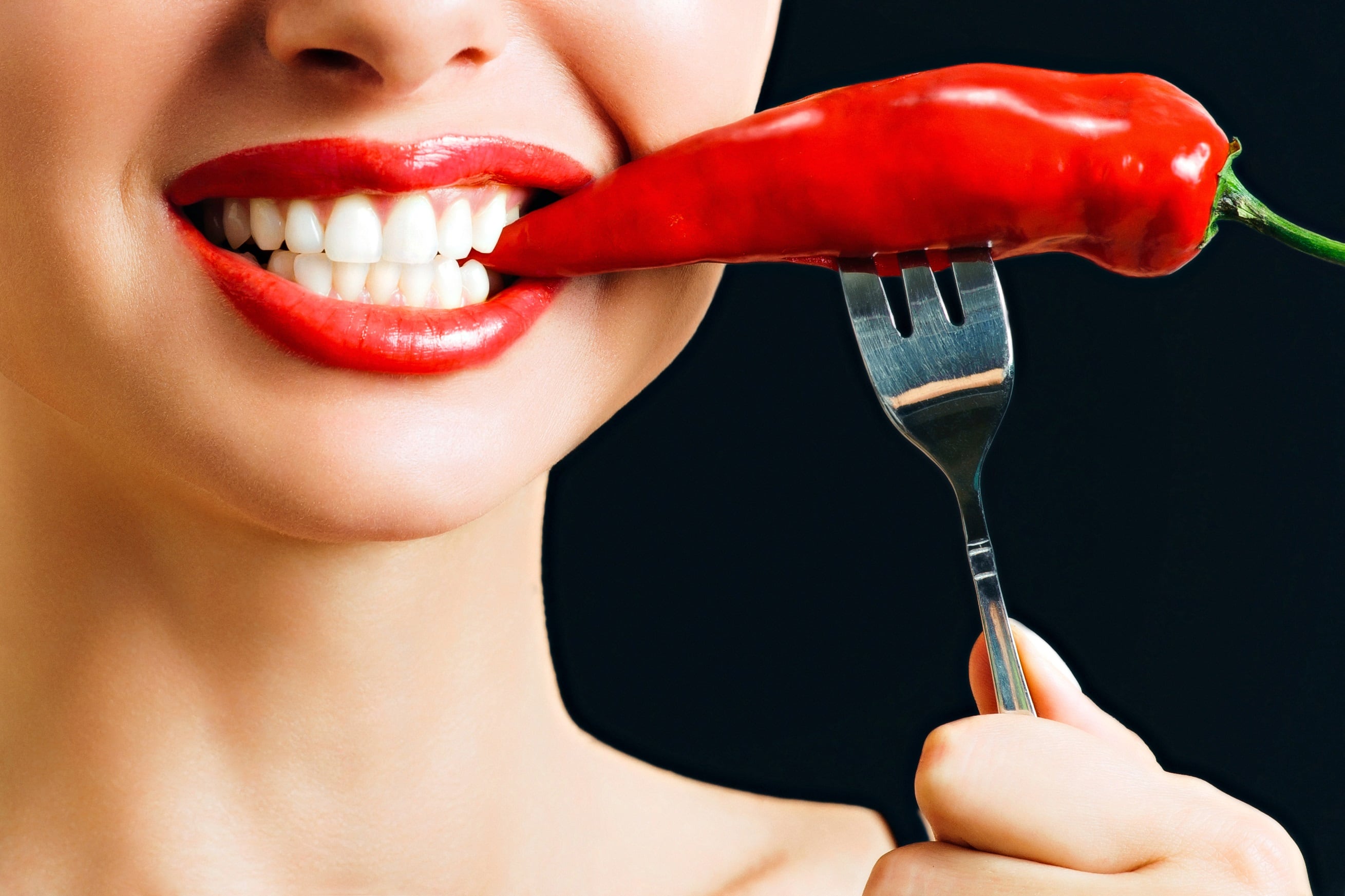 Woman eating red chili pepper isolated on black background.