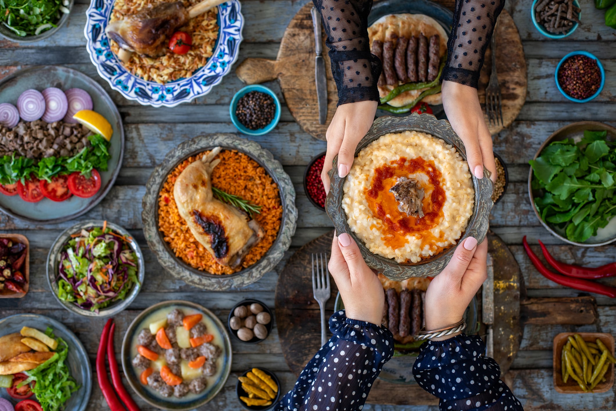 Hands of two women holding tradiitional meal harries or keşkek at the dining table with many meals.
