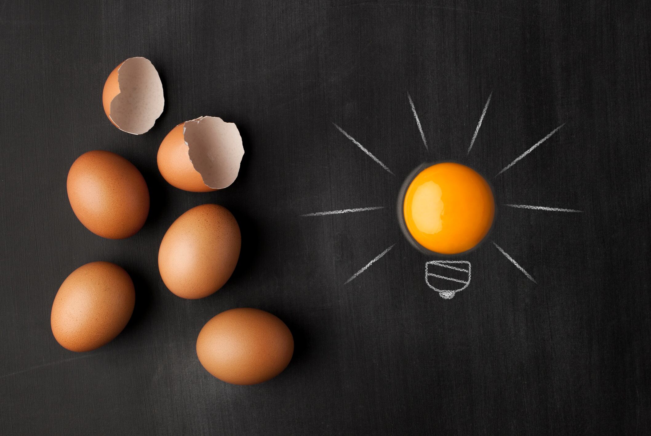 Egg yolk ball forming a shape of illuminated light bulb on blackboard