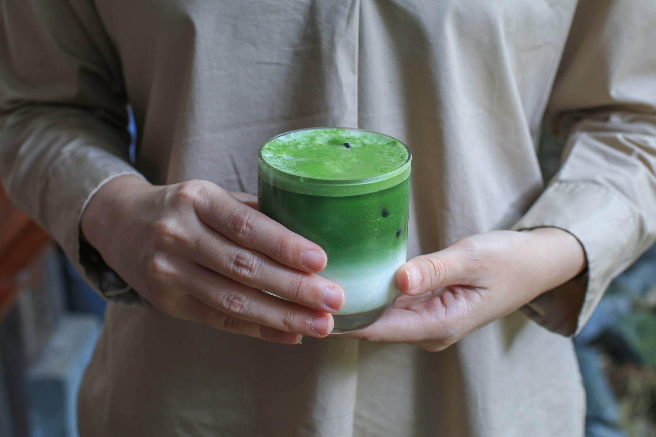 Female hand holding a glass of ice matcha green tea latte  in a beautiful minimal cafe. Organic Healthy drink.