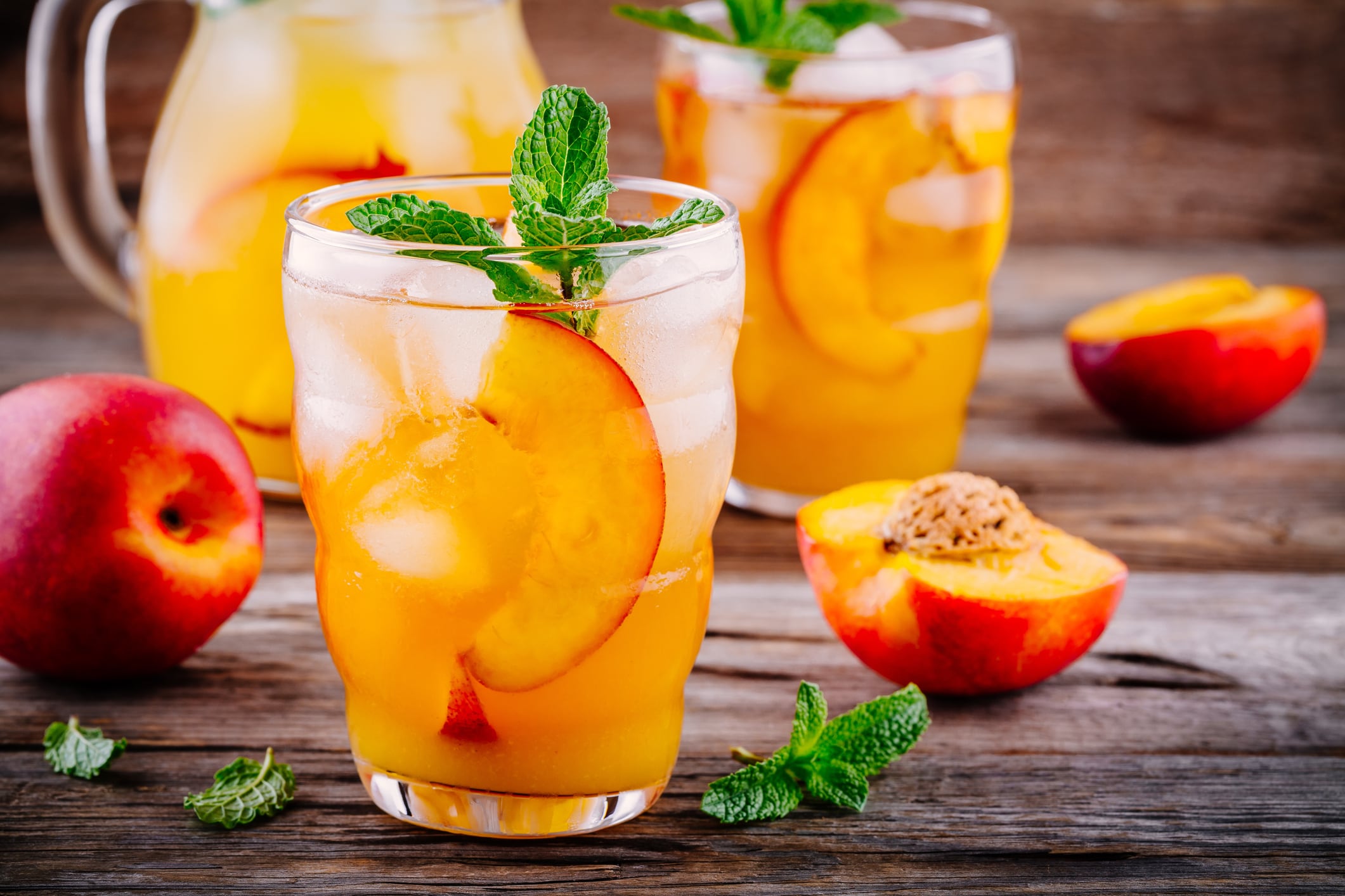 Homemade peach ice tea with ice cubes, and mint in glass on wooden background