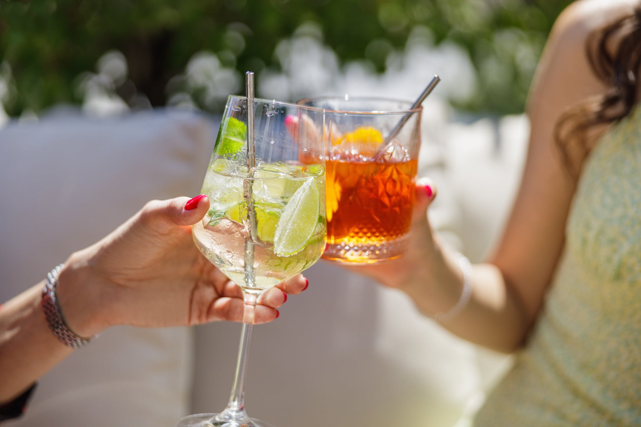 Female hands proposing a toast with glasses of yellow and red cocktail, garden cocktail party