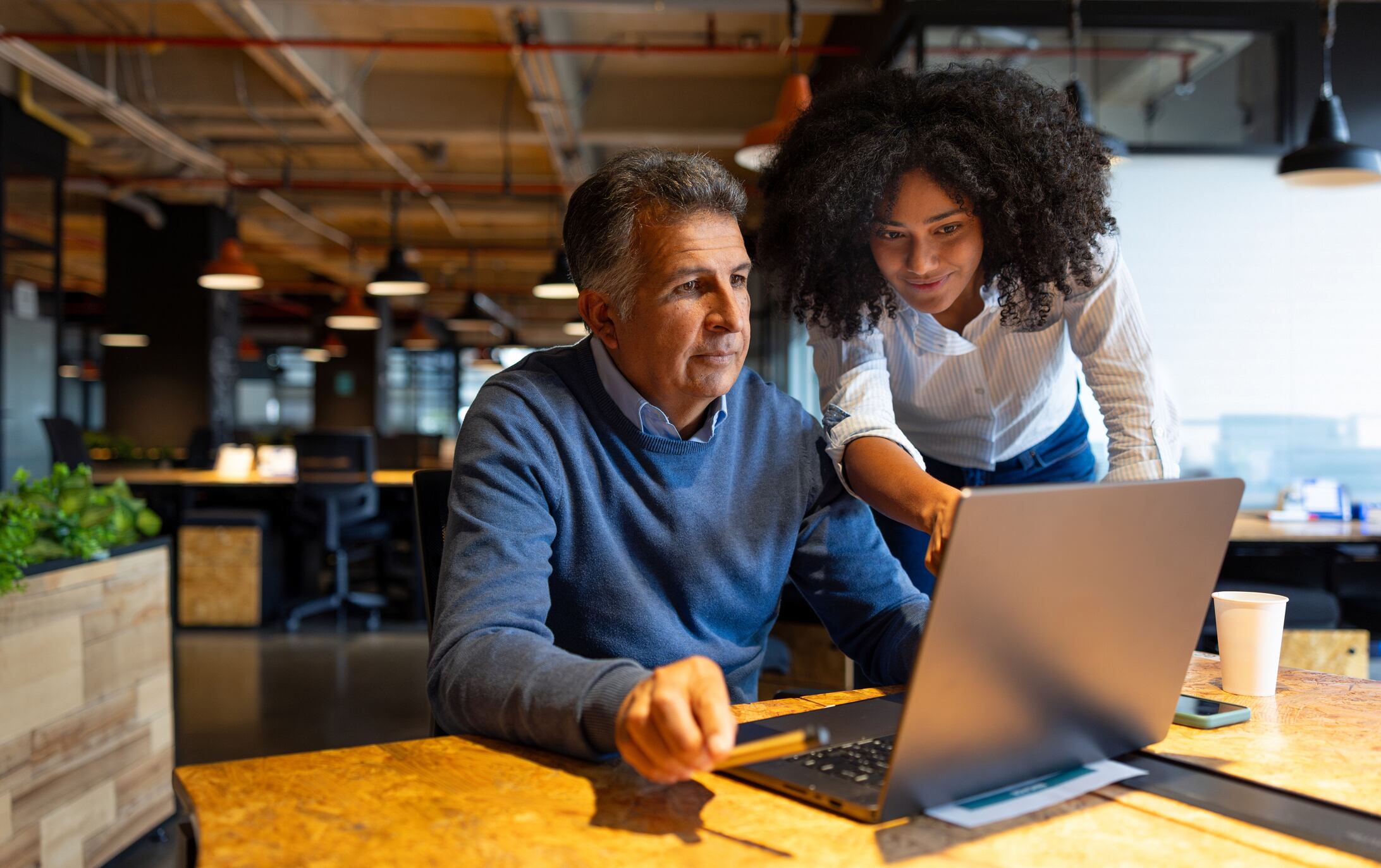 Gen Z businesswoman explaining something to a Gen X coworker on his laptop while working at the office