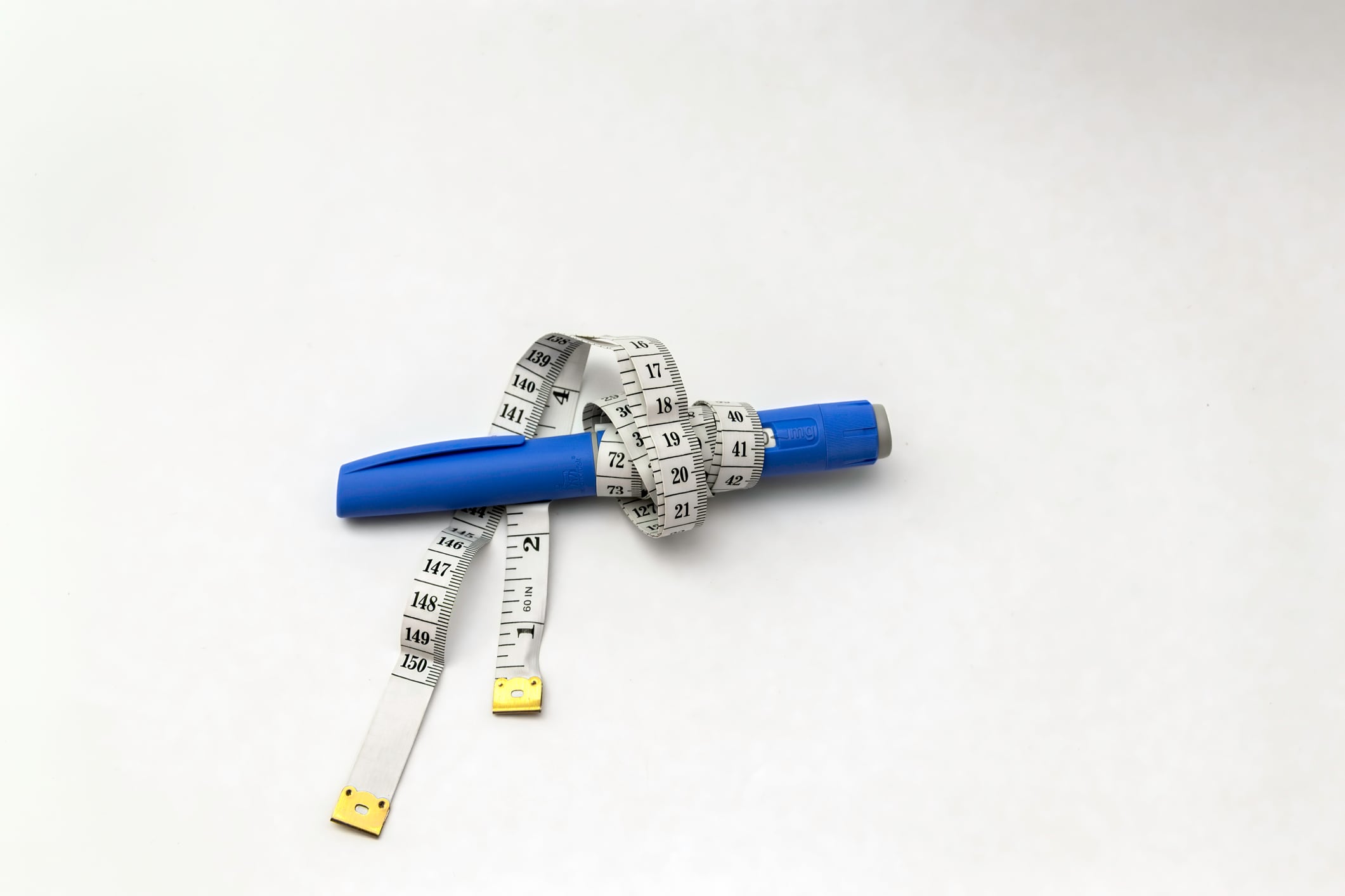 Medical injection pen wrapped with measuring tape on white background. Concept of healthcare, medical treatment, hormone therapy, diabetes management, weight control and metabolic health.