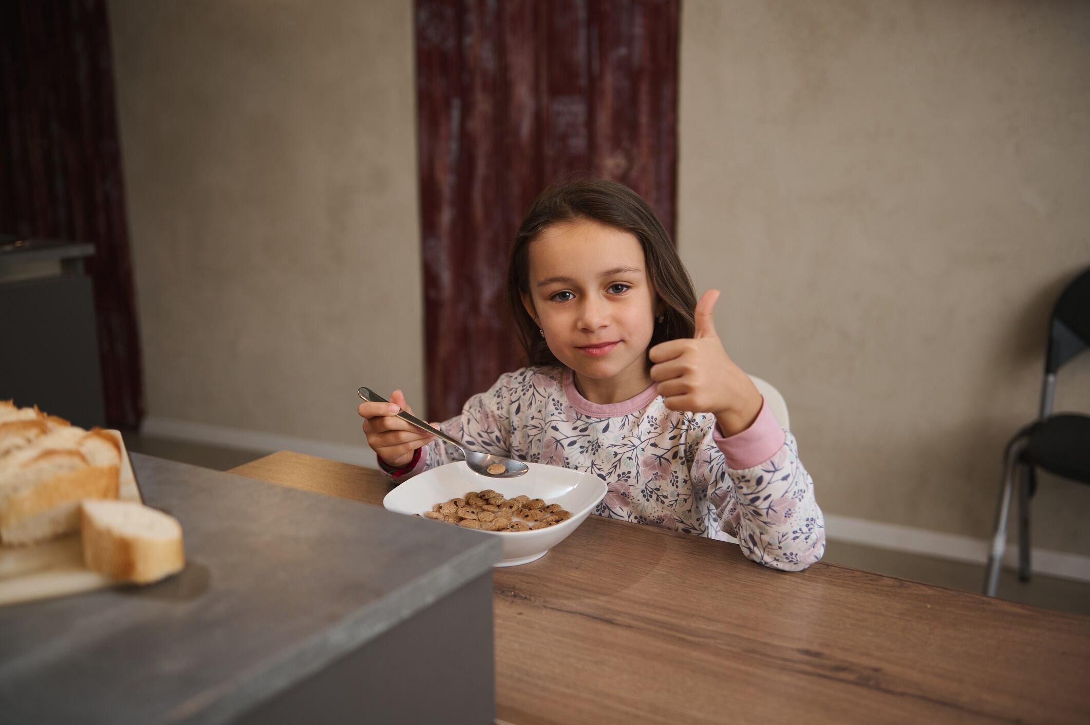 Smiling girl giving thumbs up while eating breakfast cereal at home