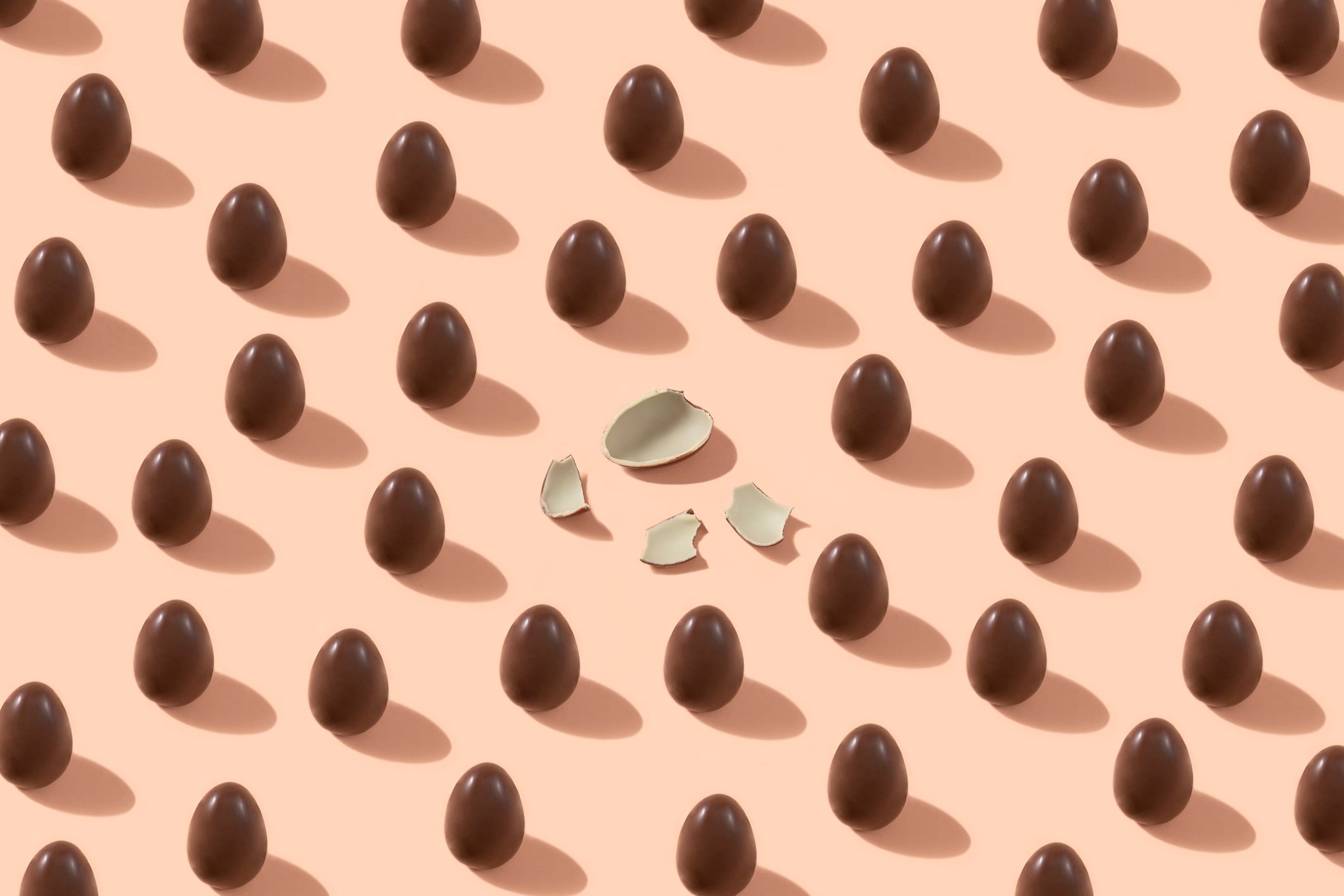 Chocolate eggs placed as a pattern where one has cracked on pink background.