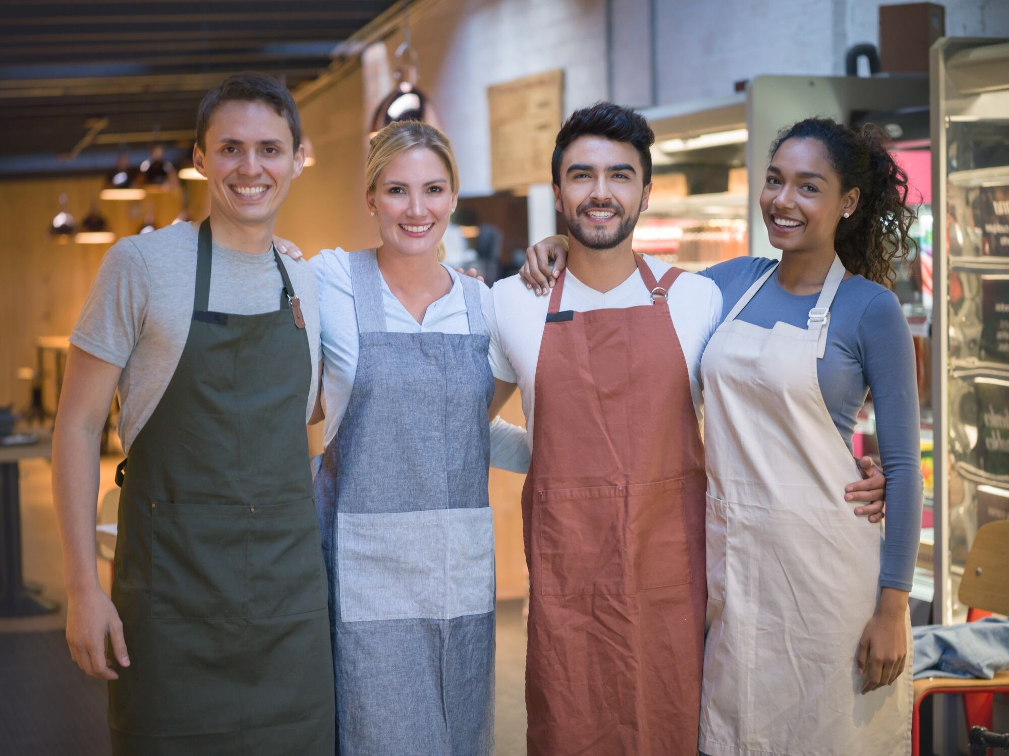 Portrait of diverse team working at a food store all looking at camera smiling very happy while embracing each other