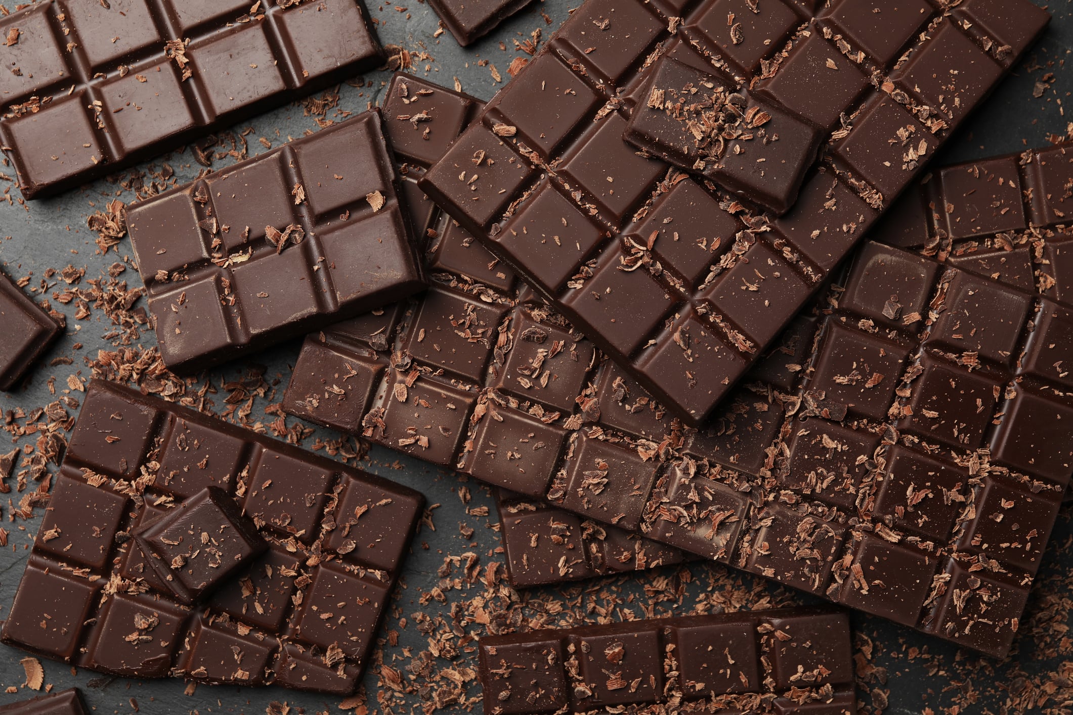 Pieces and shavings of tasty chocolate bars on grey table, flat lay