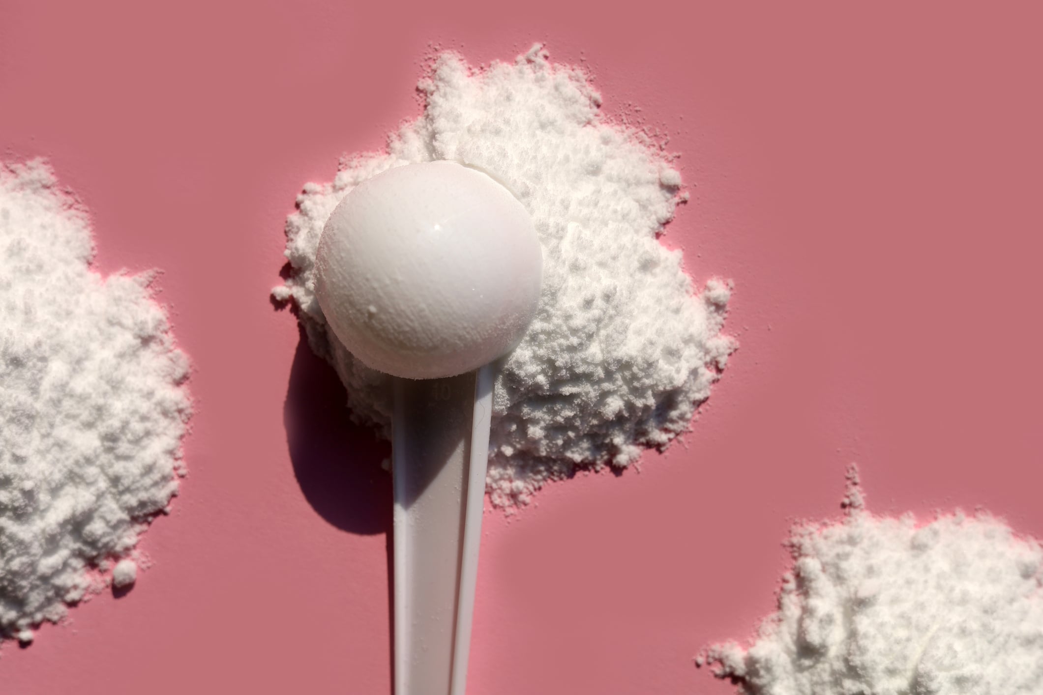 White creatine powder on pink background.