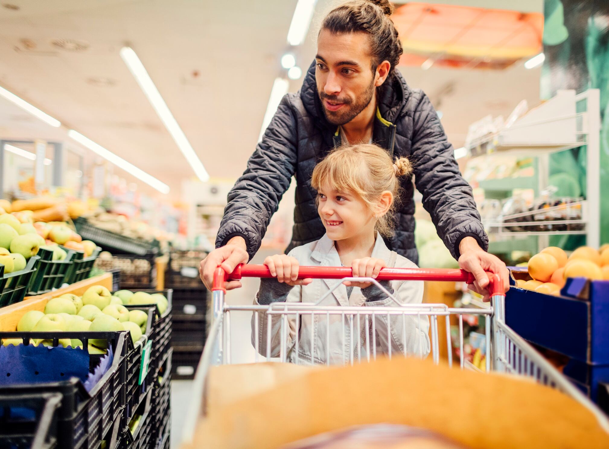 Father and his 6 years old daughter in groceries shopping. They are walking trough fruit department and talking. Pushing shopping trolley.