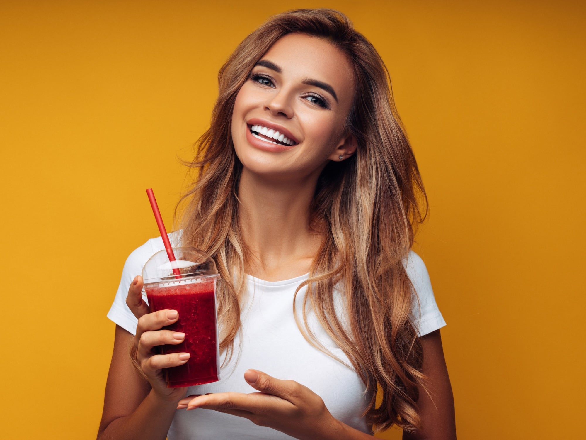 Woman holding strawberry smoothie. Yellow background.