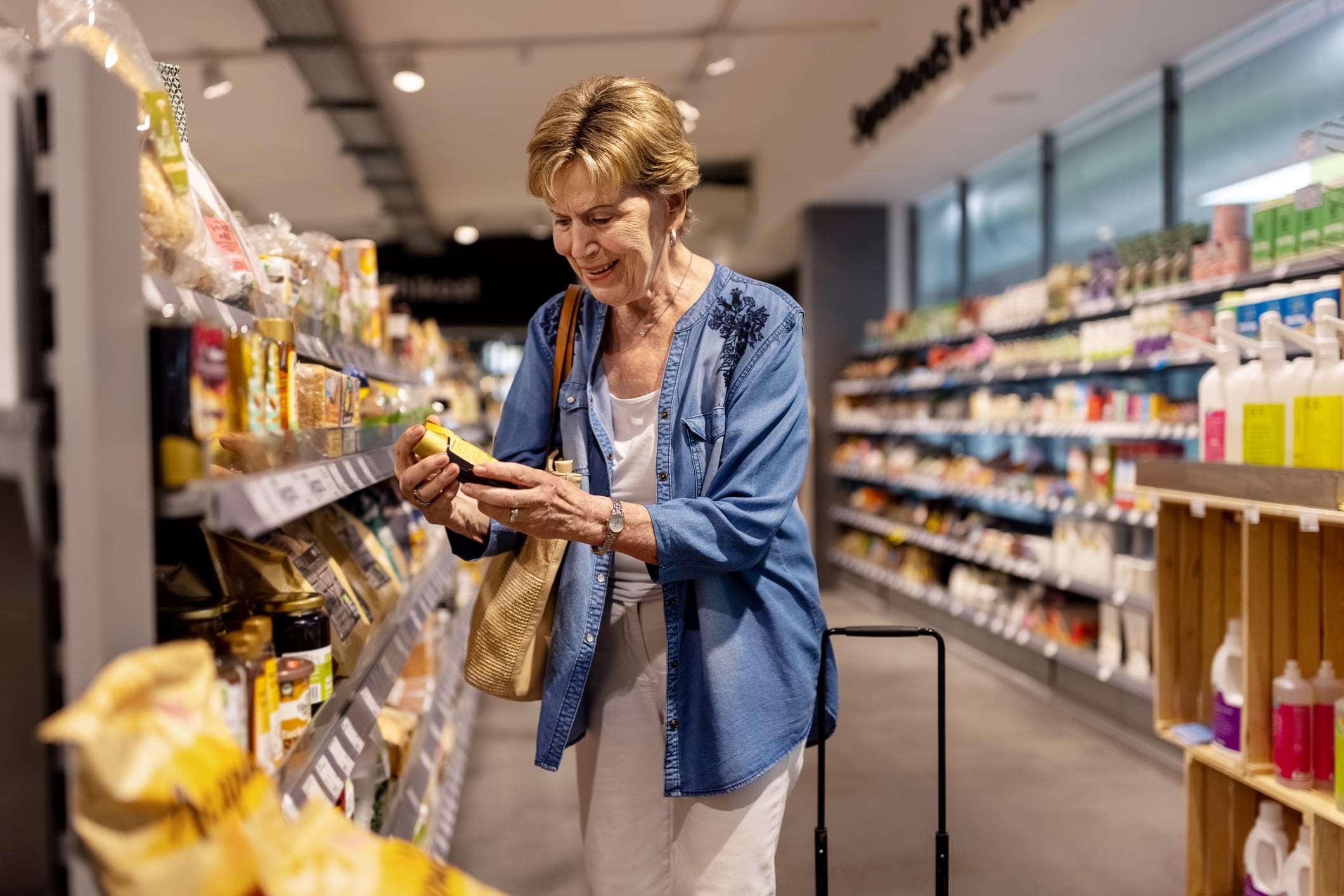 Elderly woman buying grocery products in supermarket. Elderly female shopping in the grocery store. Woman reading product details on label in store.