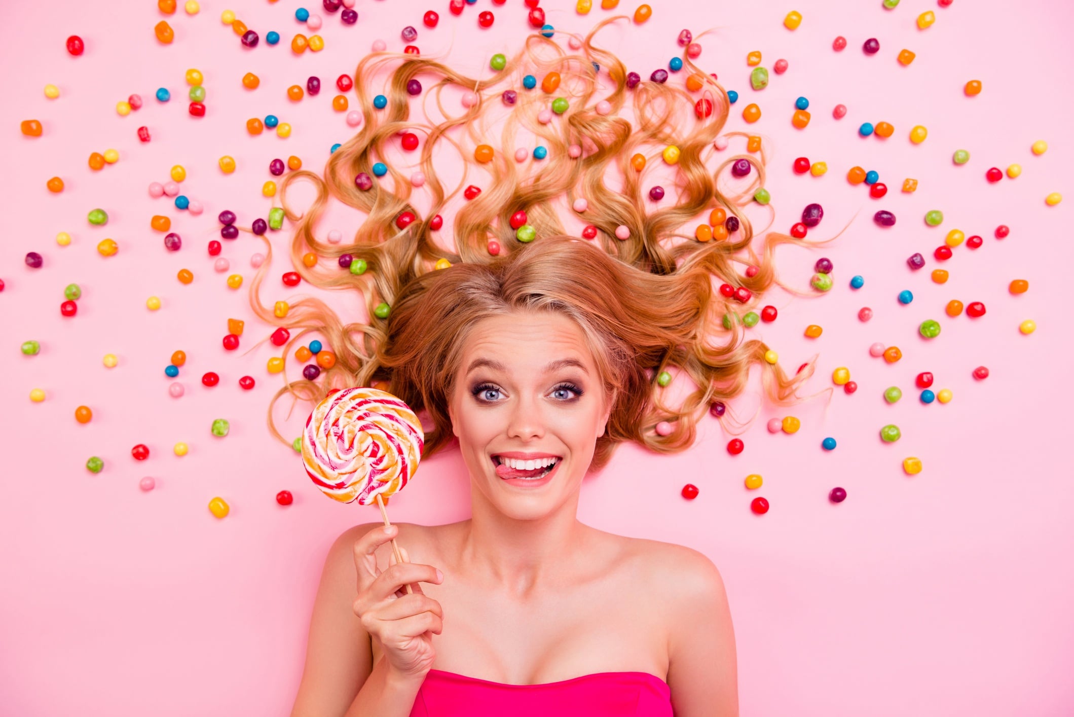 Woman lying on the floor, holding a lollipop and surrounded by sweets.