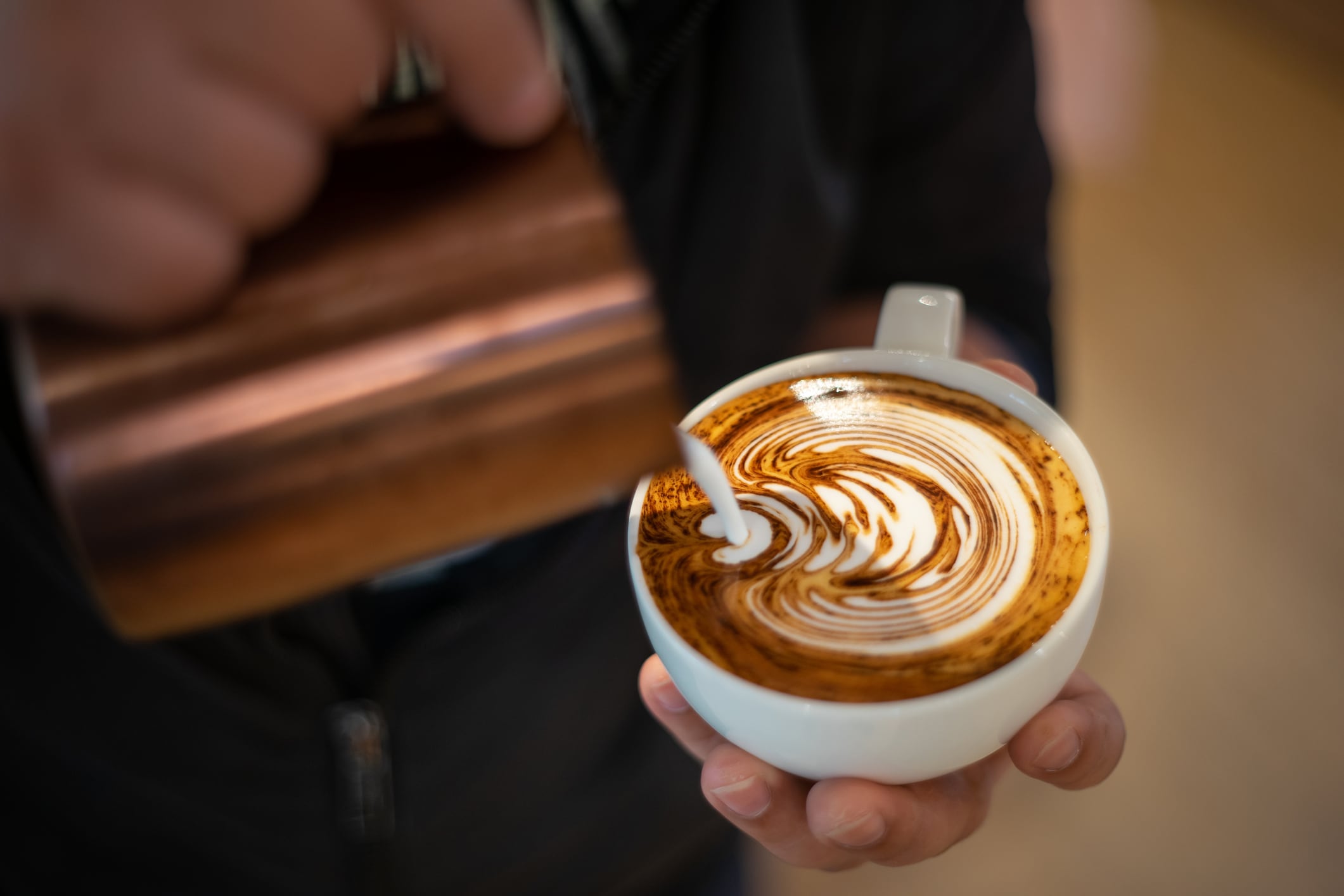 barista hands, preparing proper cappuccino pouring Milk into a glass of coffee.