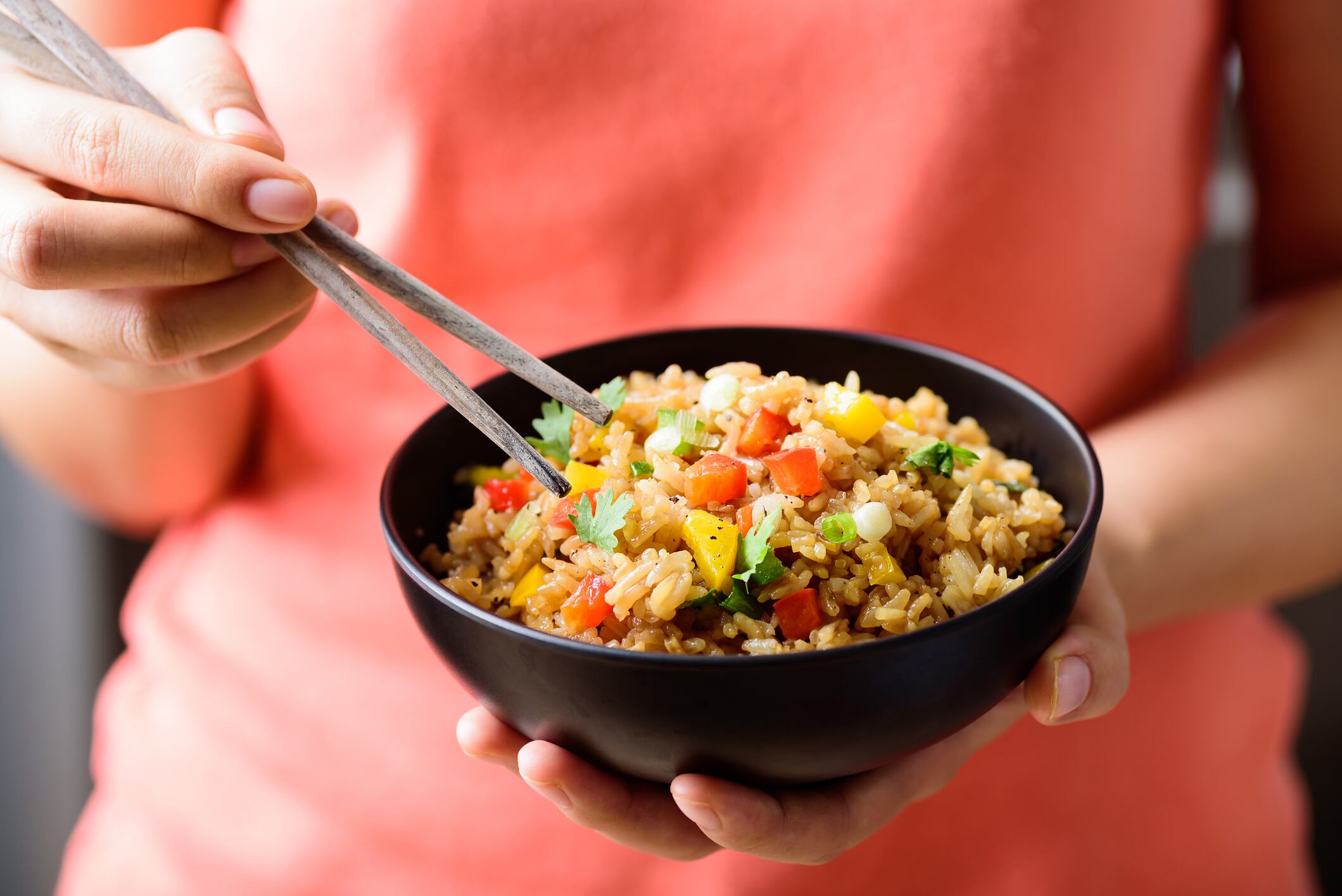 Hand holding chopsticks for eating fried rice with vegetables in a bowl, Asian food