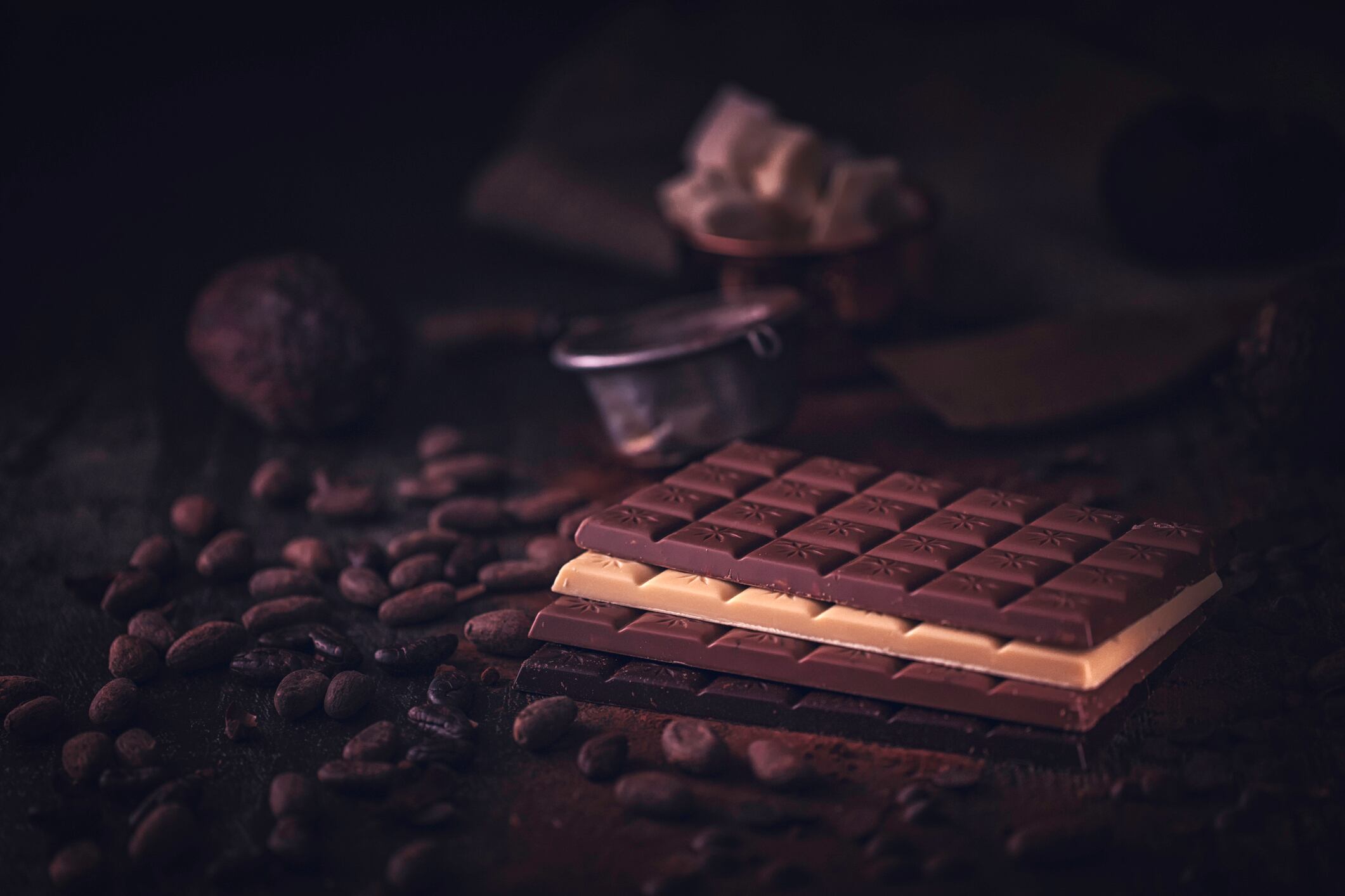 Three chocolate bars - white, milk and dark - surrounded by cocoa beans.