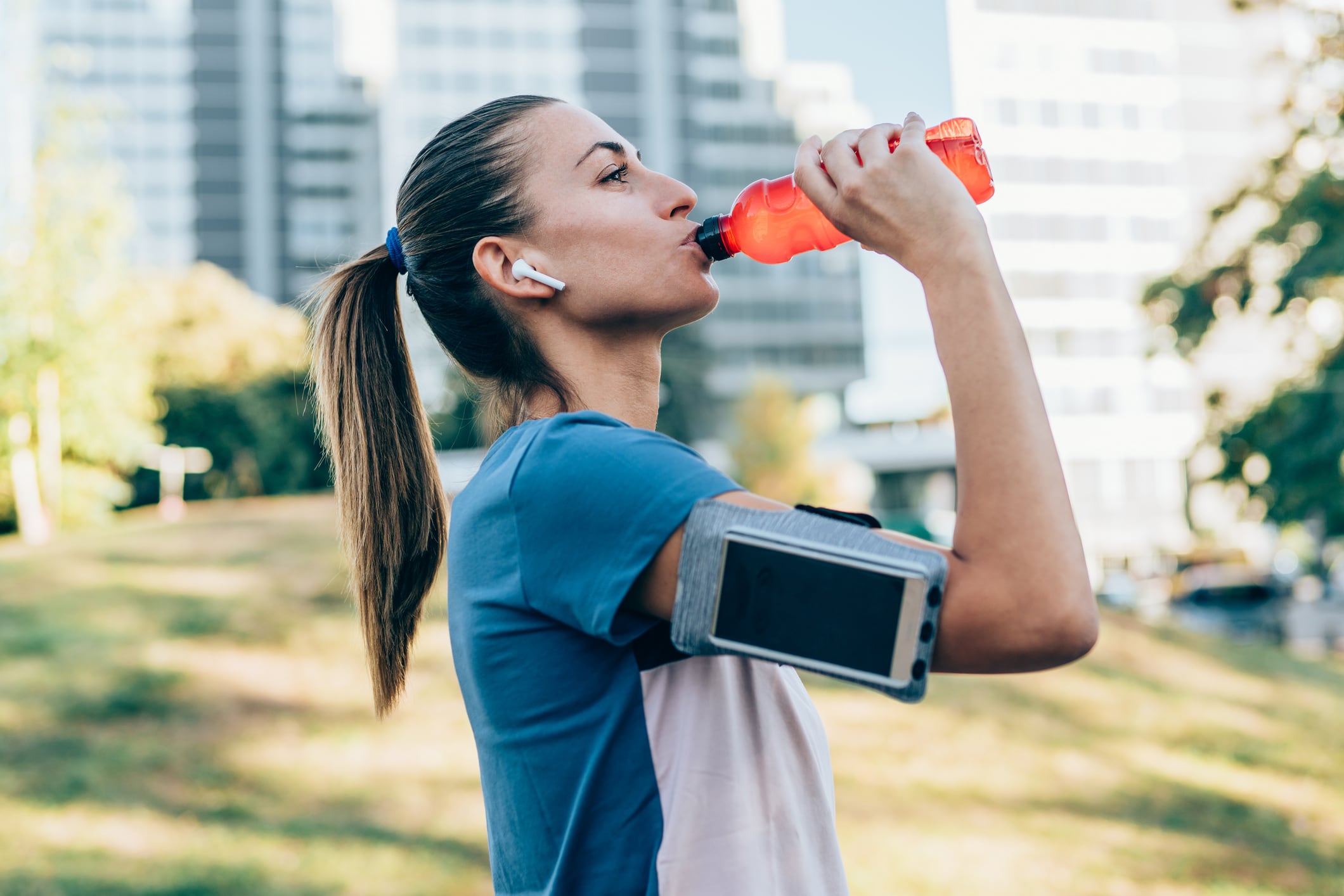 Sporty woman drinking water from bottle after exercising outdoors. Beautiful young woman sipping water from pink bottle after workout at park.
