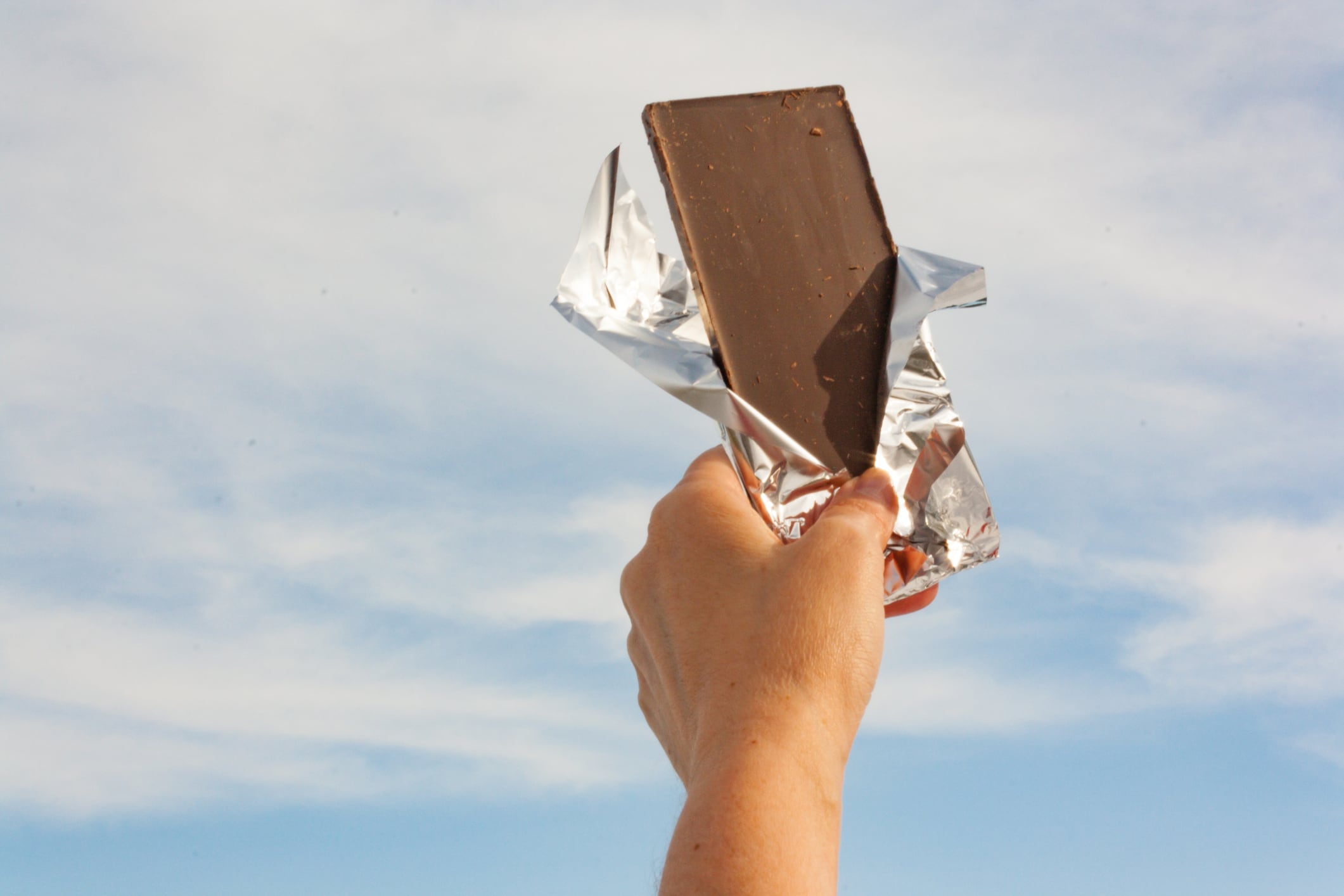 Hands of a woman holding a tile of chocolate against the sky