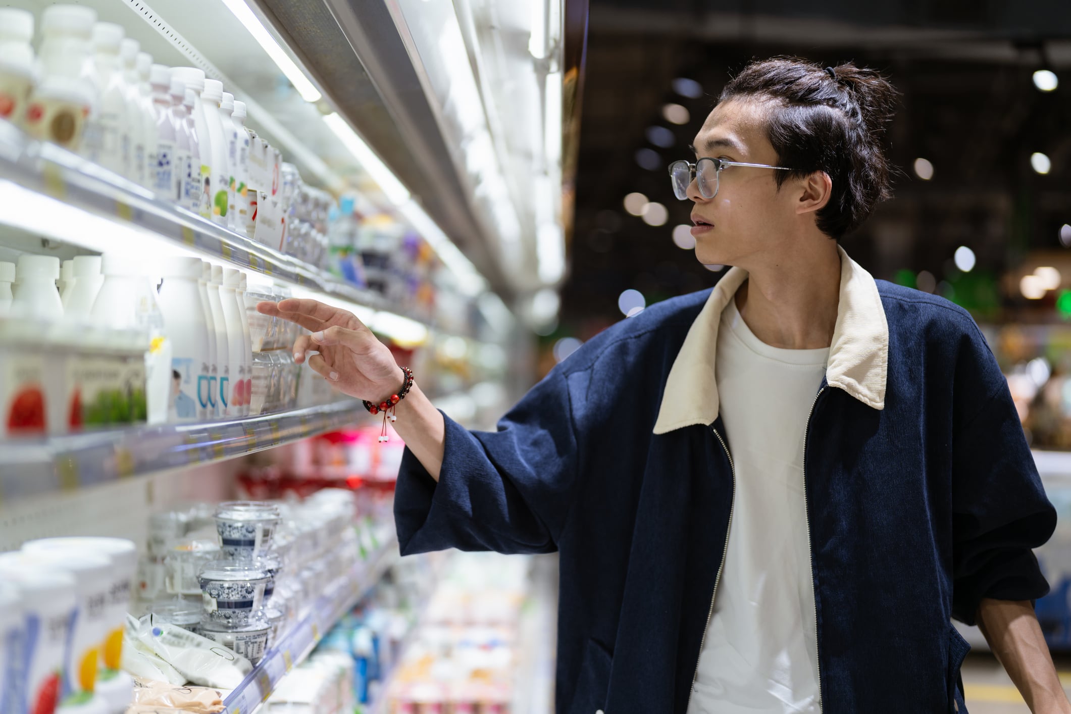 A young man selecting dairy items in a well-lit supermarket aisle, showcasing concentration and intent, ideal for retail, shopping, consumer behavior themes.