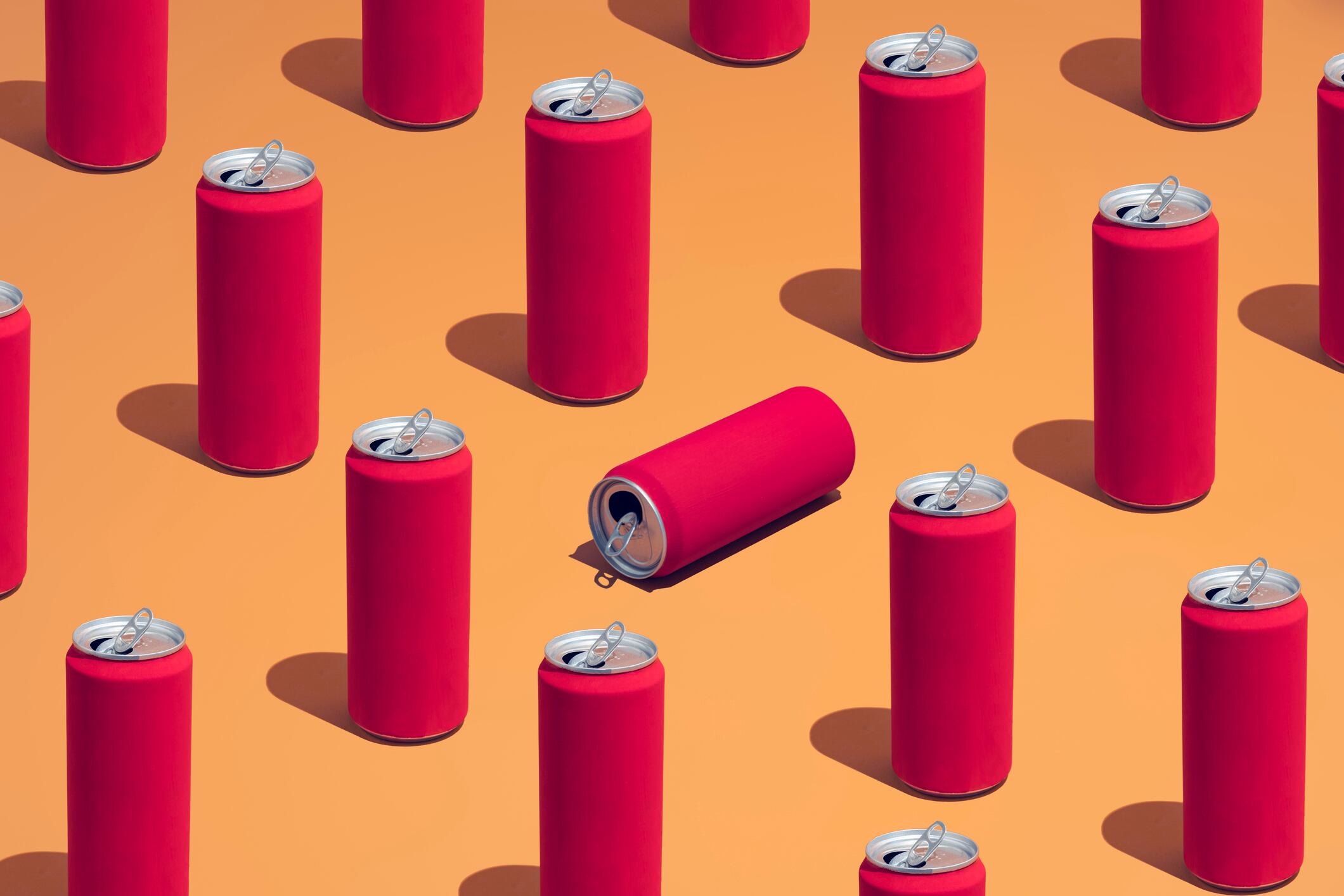 A group of red cola cans laid in a repetative pattern on a colorful background