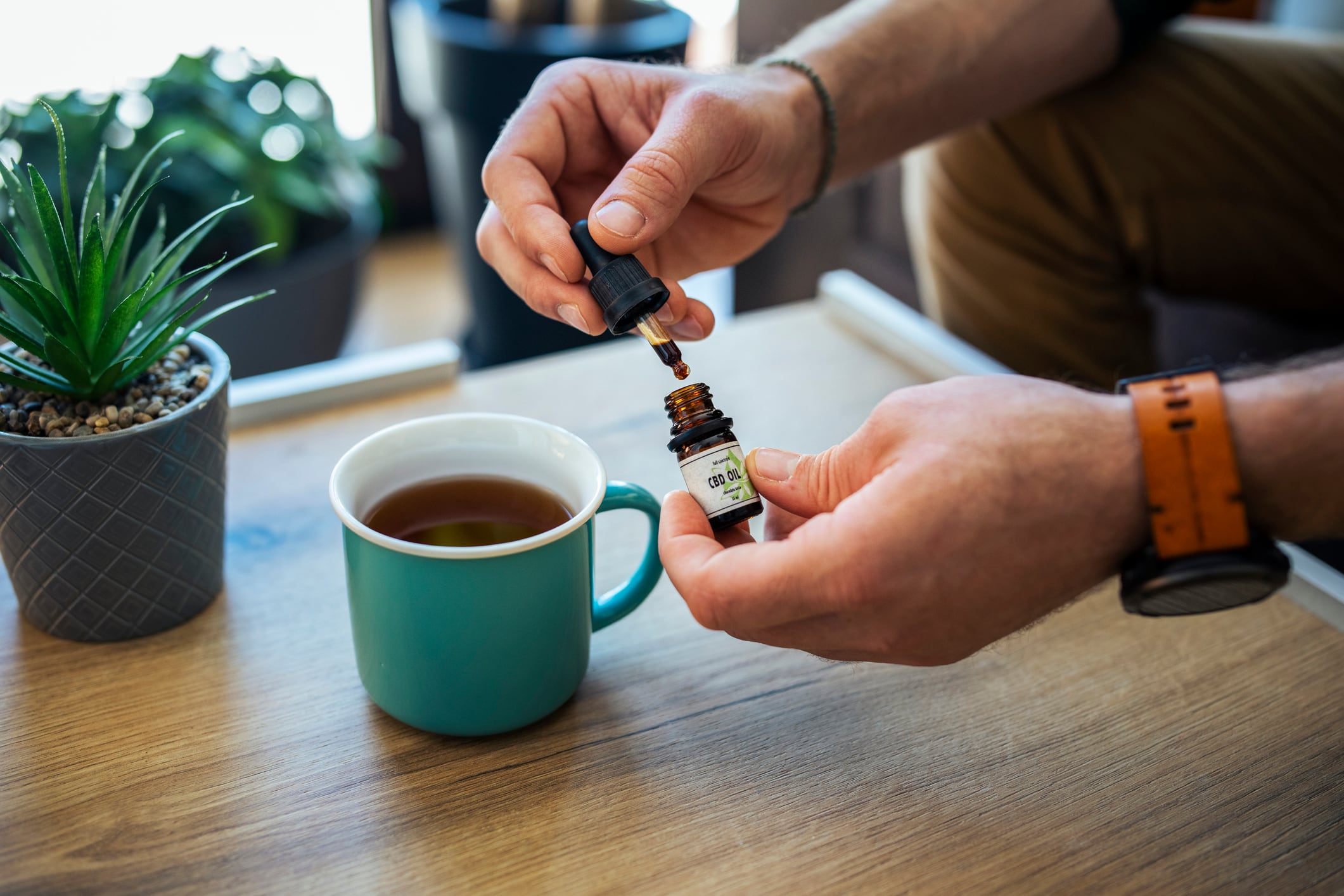 Unrecognizable man dropping cbd oil in his herbal tea.