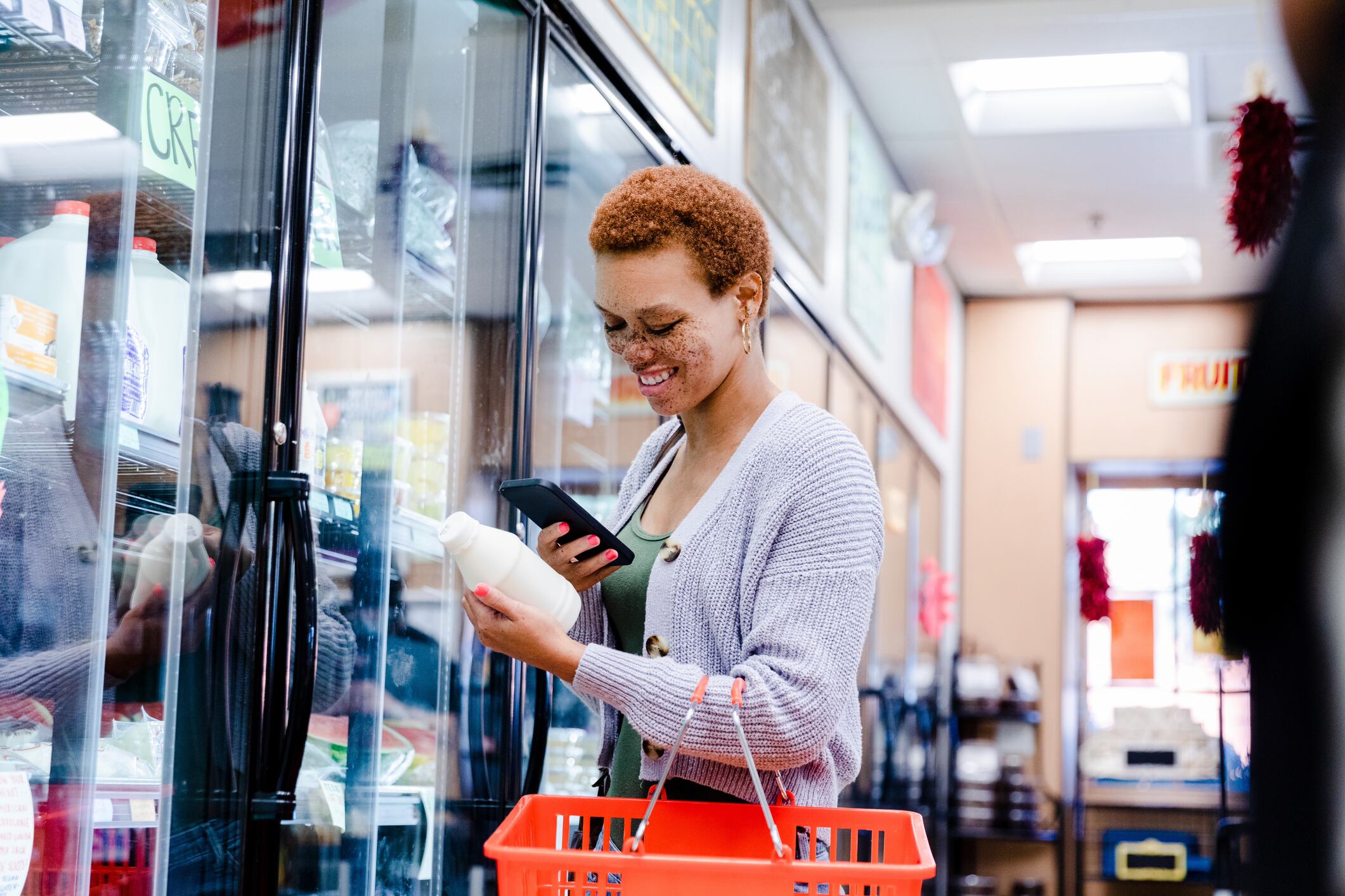 The smiling mid adult woman uses a mobile app on her smart phone to scan the label on the milk container at the market.