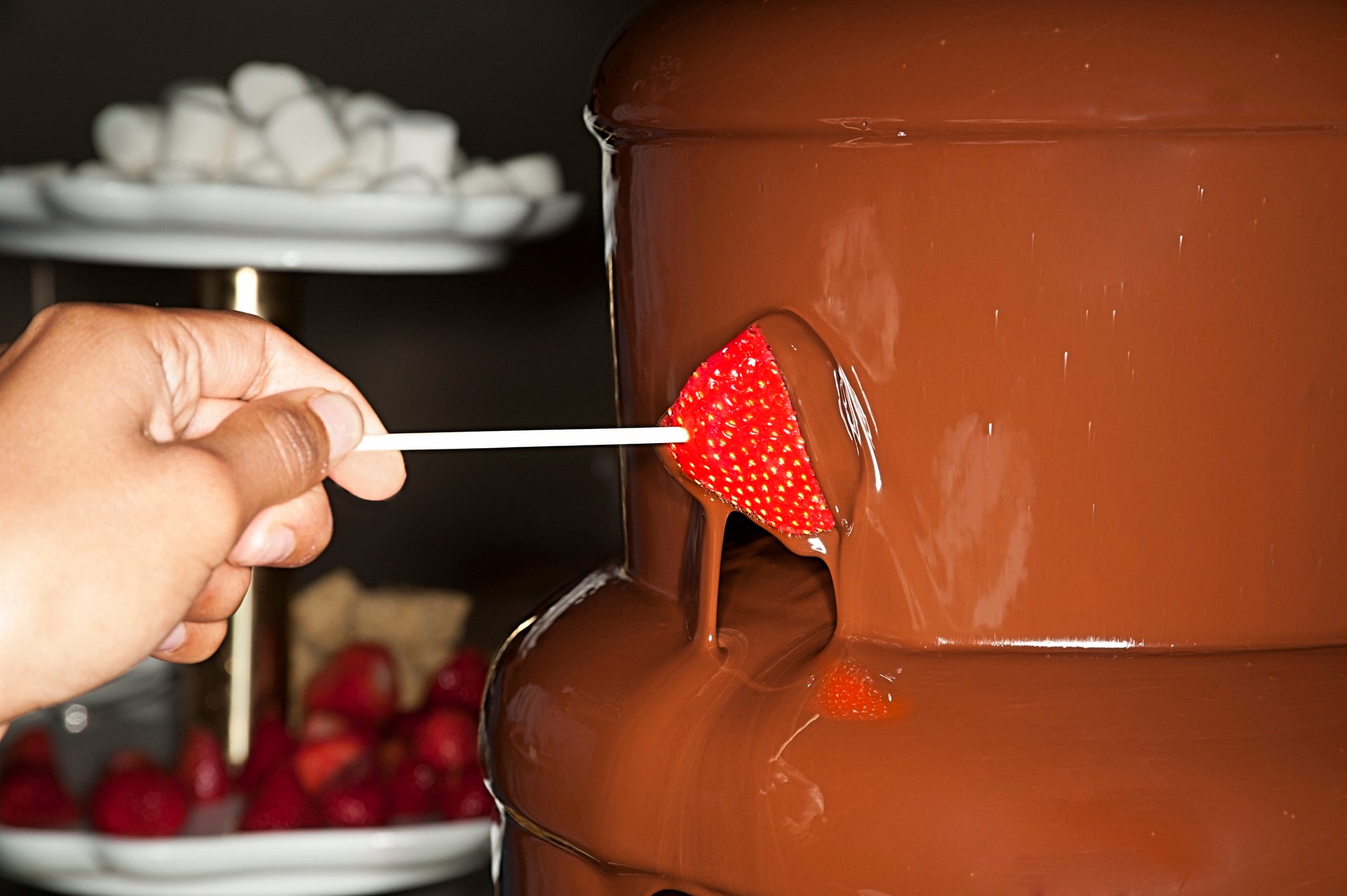 Chocolate fountain, with a strawberry being coated by the running chocolate.