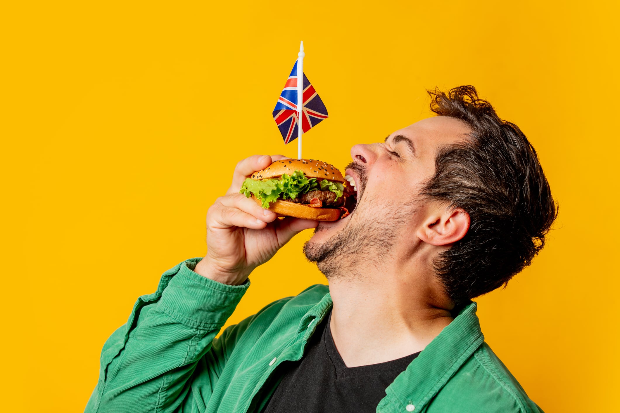 Smiling man with Great Britain flag and burger on yellow background