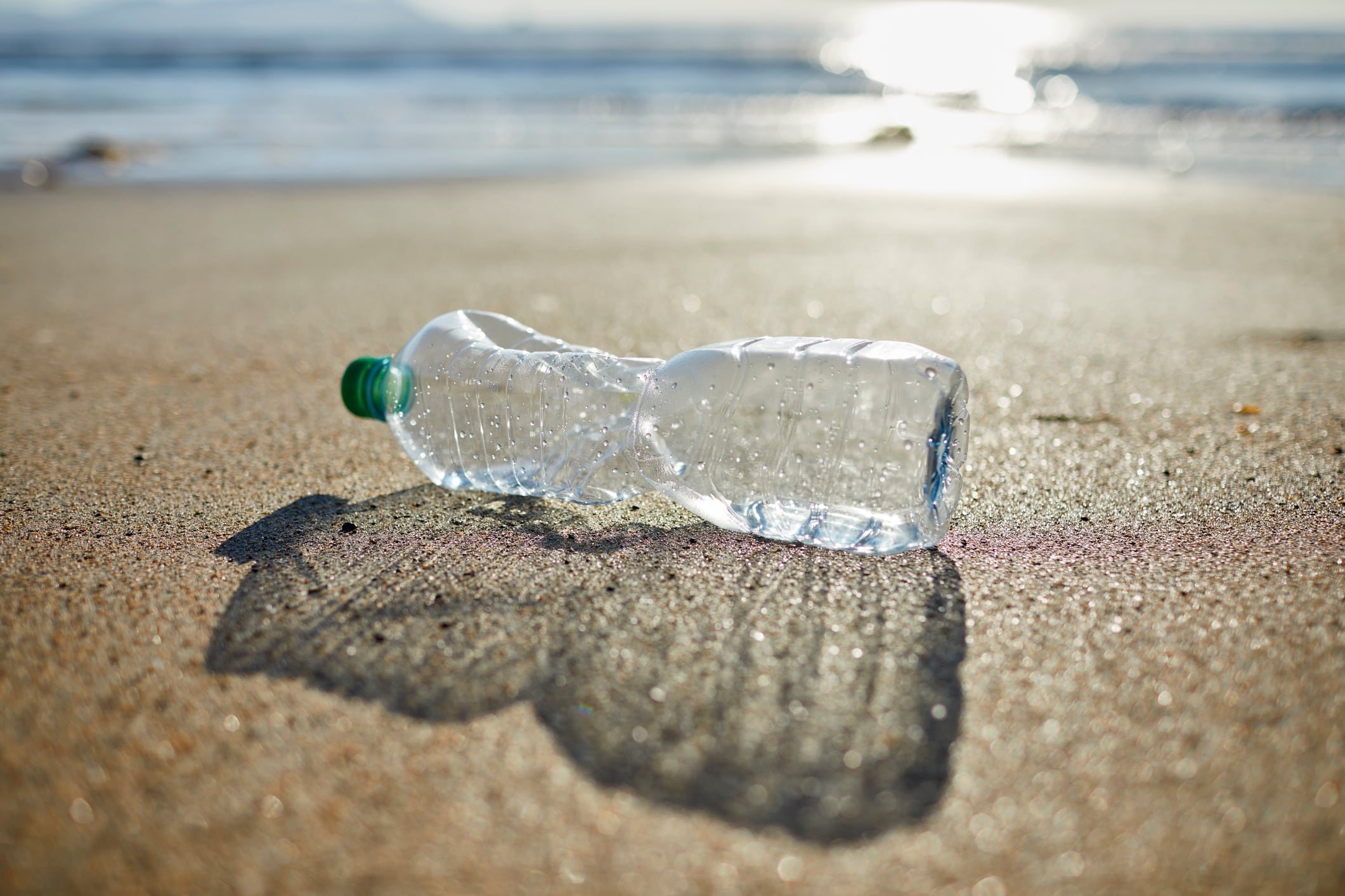 Close-up of empty plastic bottle on shore. Abandoned waste is on sand. Garbage is polluting beach.