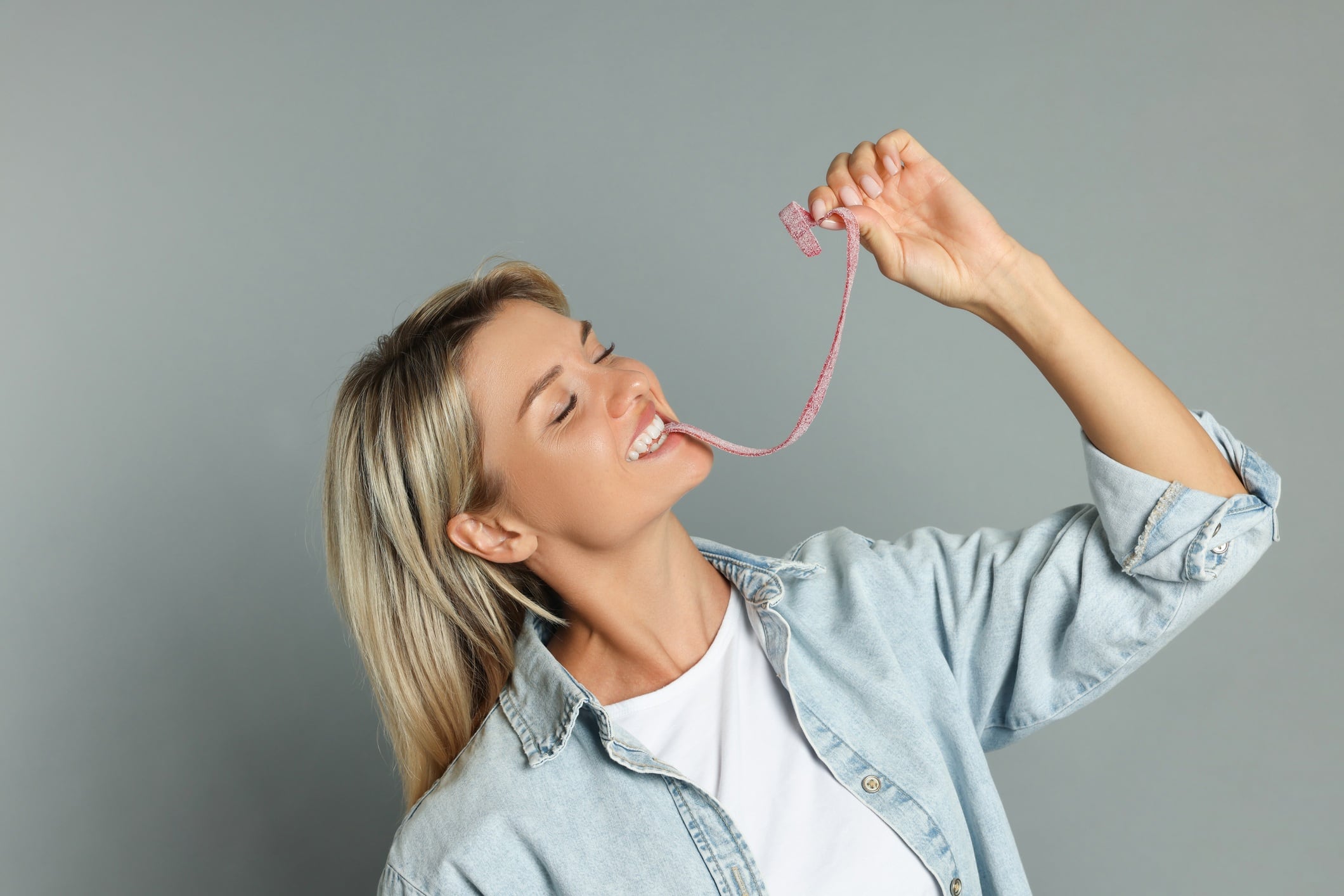 Woman eating gummy candy on grey background.