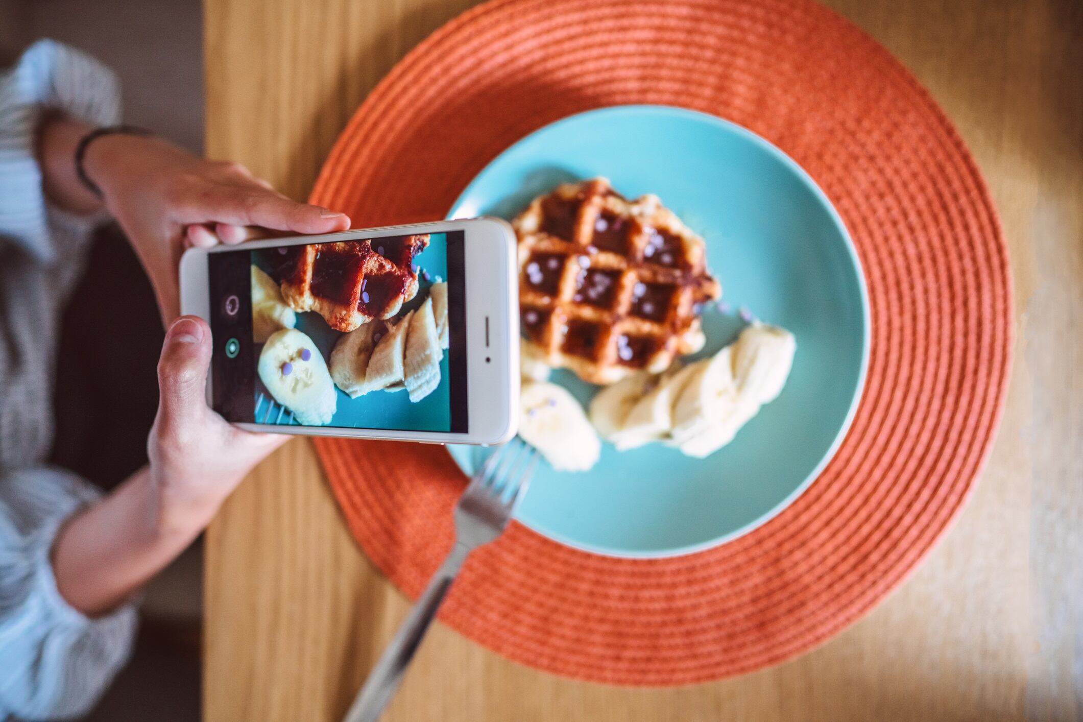 Teenage girl taking photo of her homemade dessert with smartphone at dining table at home.