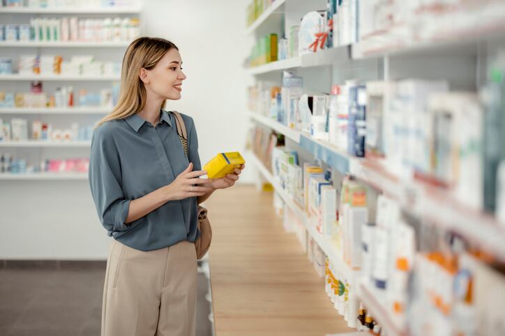 A young female shopper selecting products at a pharmacy, reflecting the growing consumer interest in holistic wellness, simplified nutrition, and personalized health solutions.