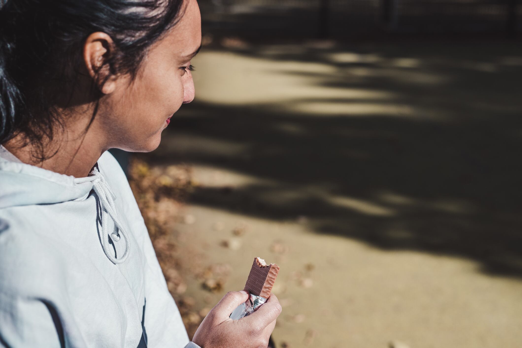 Woman eating protein bar snack after training outdoor.
