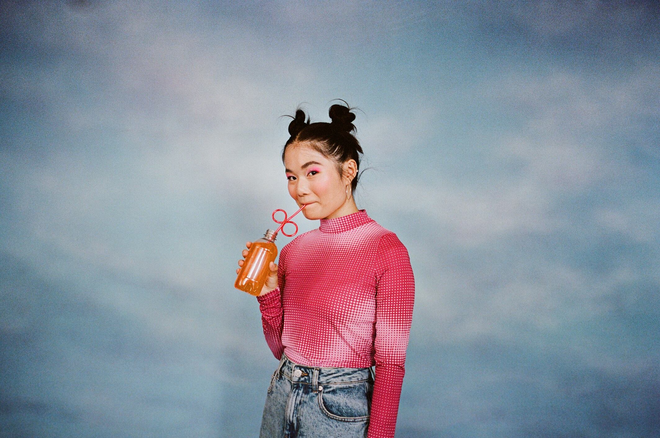 Portrait of young woman drinking juice from bottle while standing against colored background